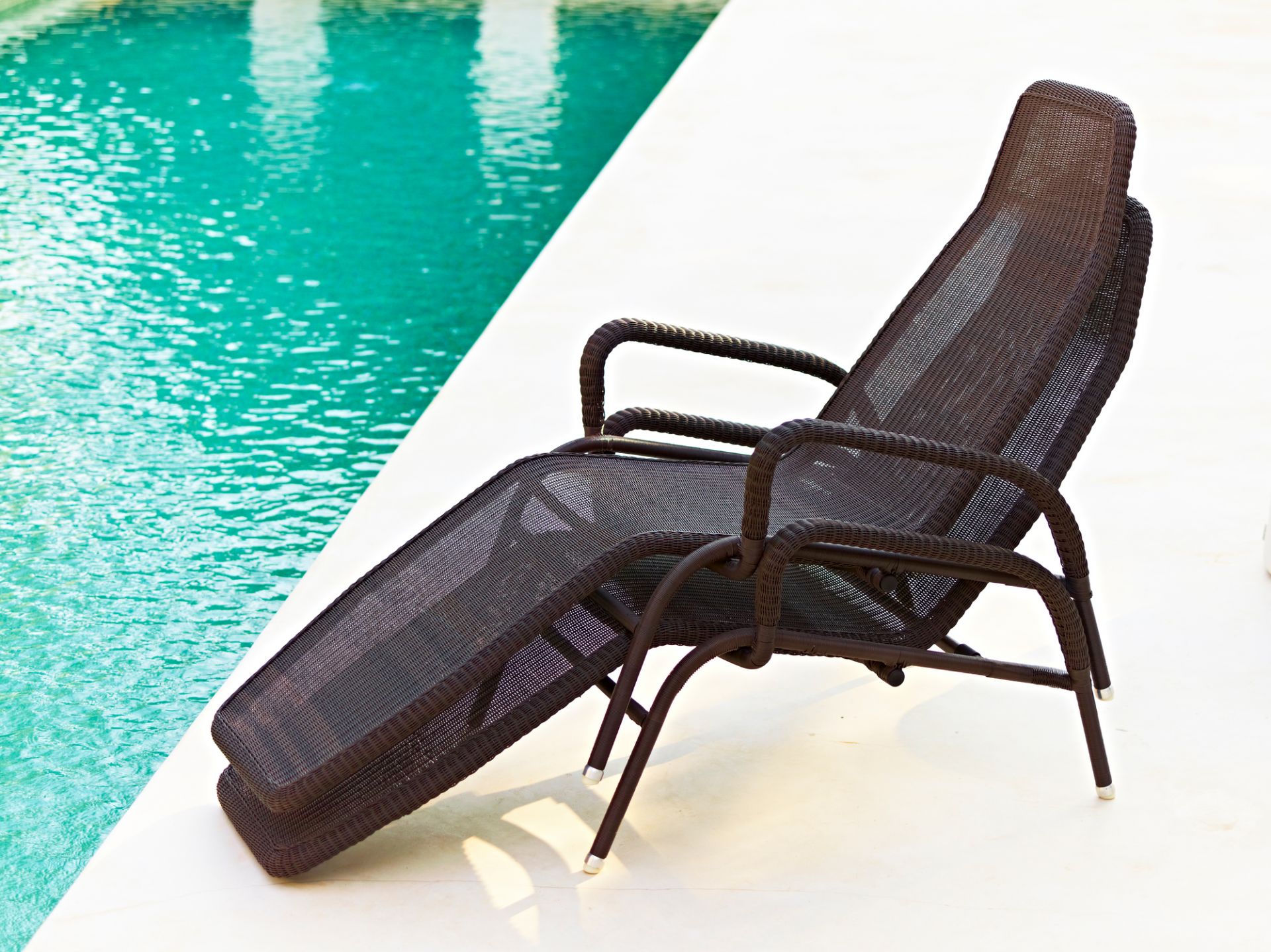 Braune Cane-Line Sonnenliege "Sunrise" aus Rattan am Pool, stapelbar und wetterfest für den Garten.