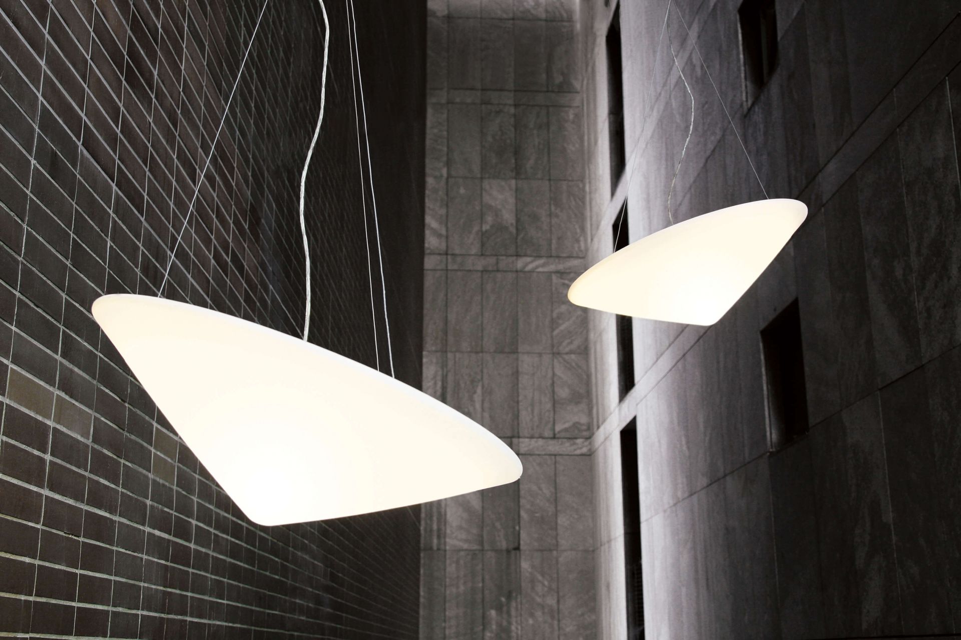 Zwei Cao Mao Pendelleuchten, modernes Design, weiße Leuchtenkörper, hängen vor einer dunklen Wand.