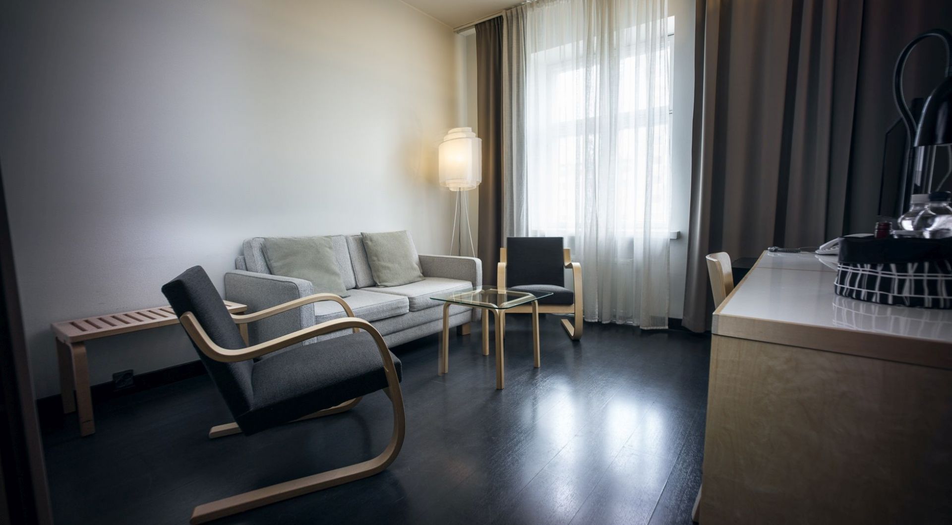 Wohnzimmer mit grauer Artek Bank, Sesseln und Glas-Couchtisch. Skandinavisches Design für modernes Wohnen.