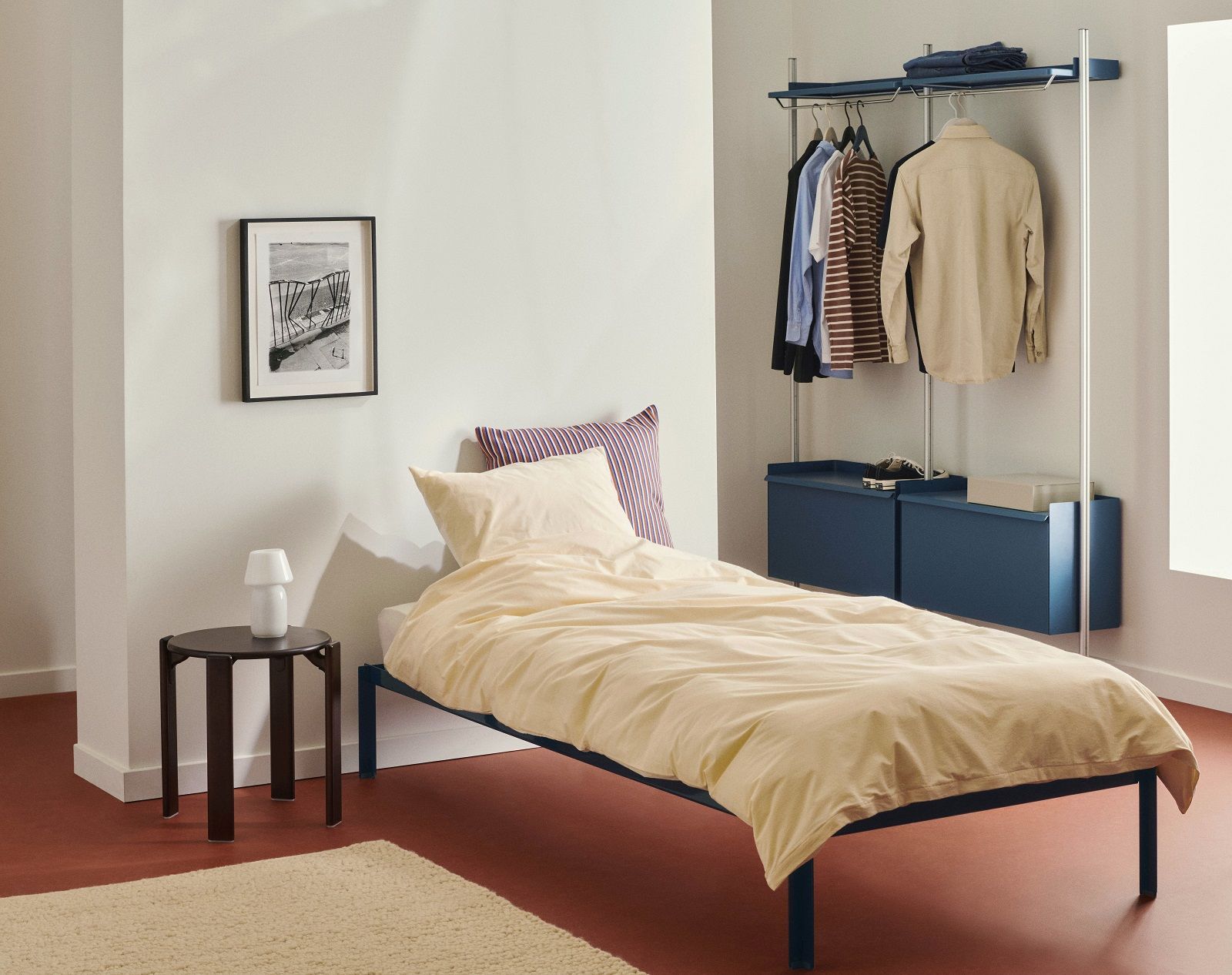 Zimmer mit Bett und Hay Pier System Regal/Garderobe in Blau mit Kleidung und Aufbewahrung.