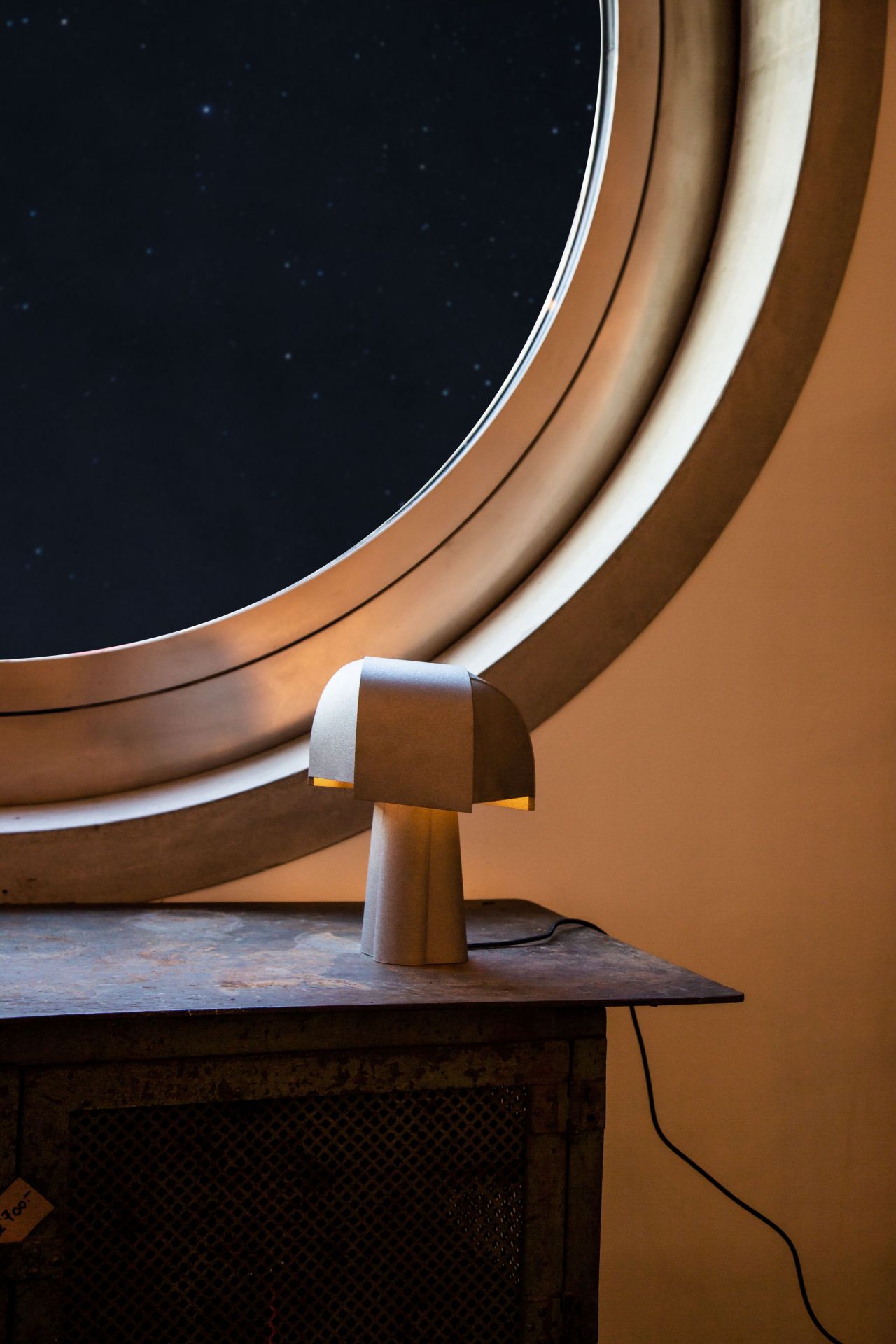 Samsa Tischleuchte von Pulpo, moderne Designleuchte aus Keramik, warmes Licht, vor rundem Fenster.