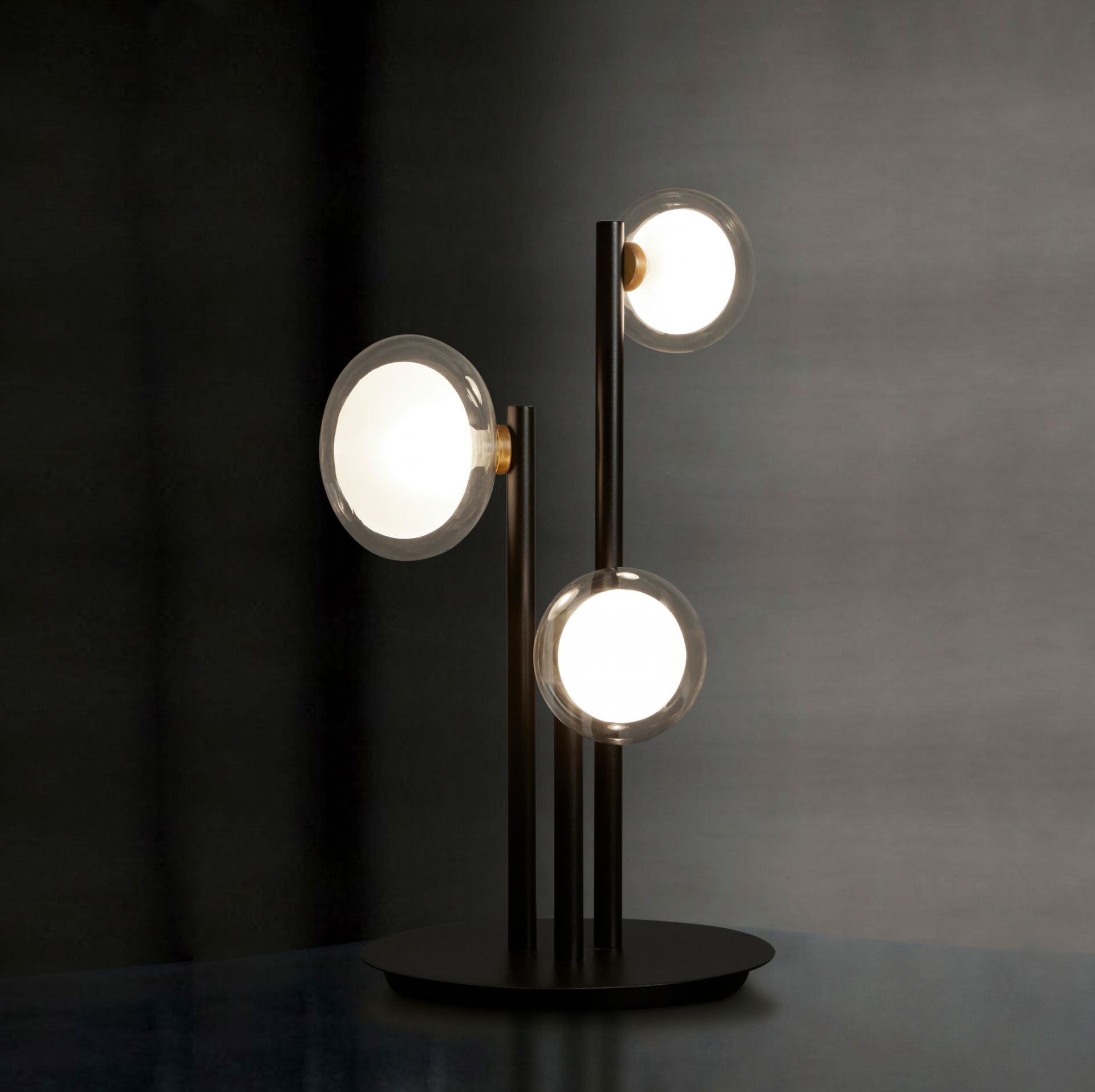 Nabila Tischleuchte von Tooy mit drei leuchtenden Glaskugeln und schwarzem Gestell.