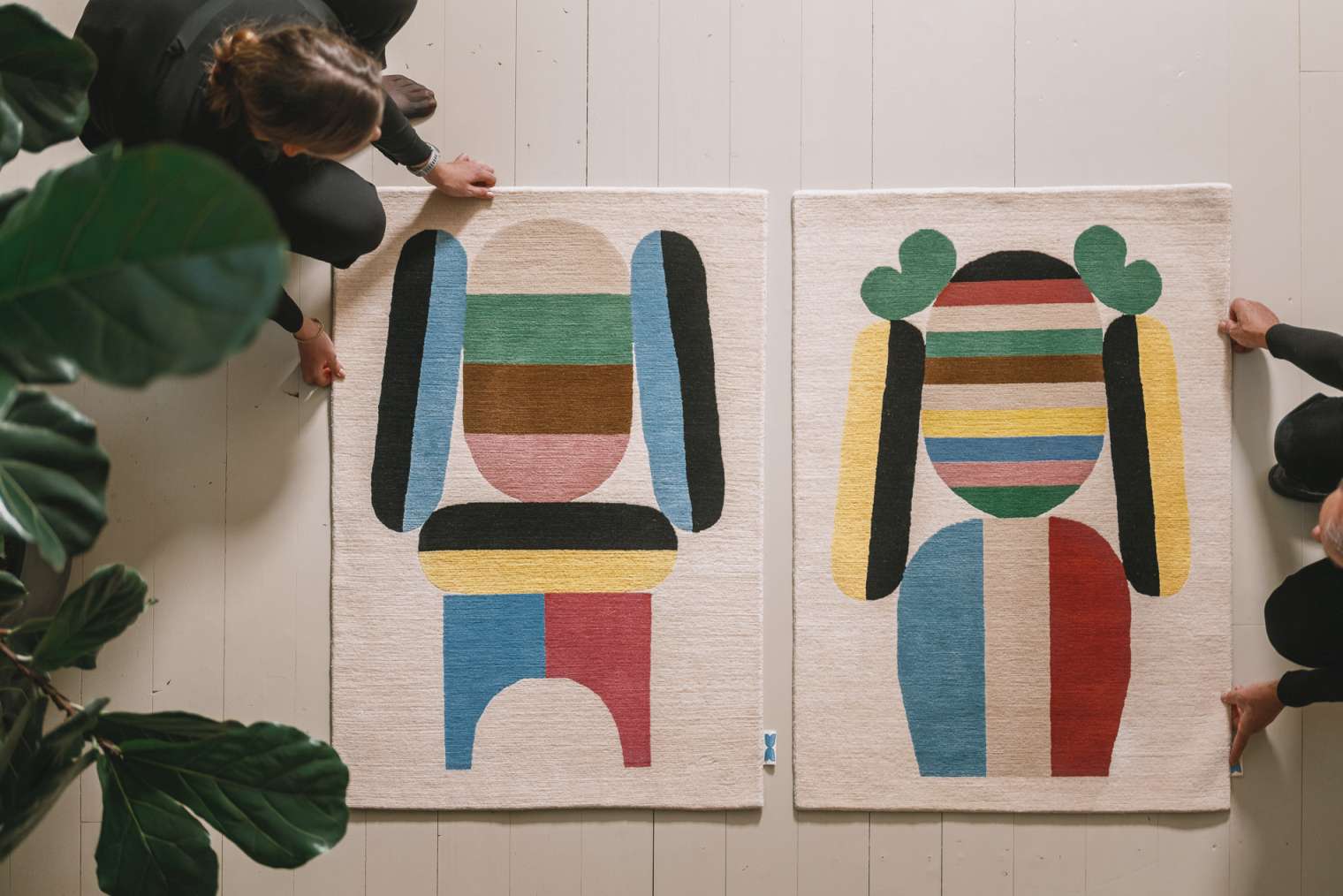 Zwei Elis Teppiche mit abstraktem, farbenfrohem Design auf hellem Holzboden, moderne Wohnaccessoires.