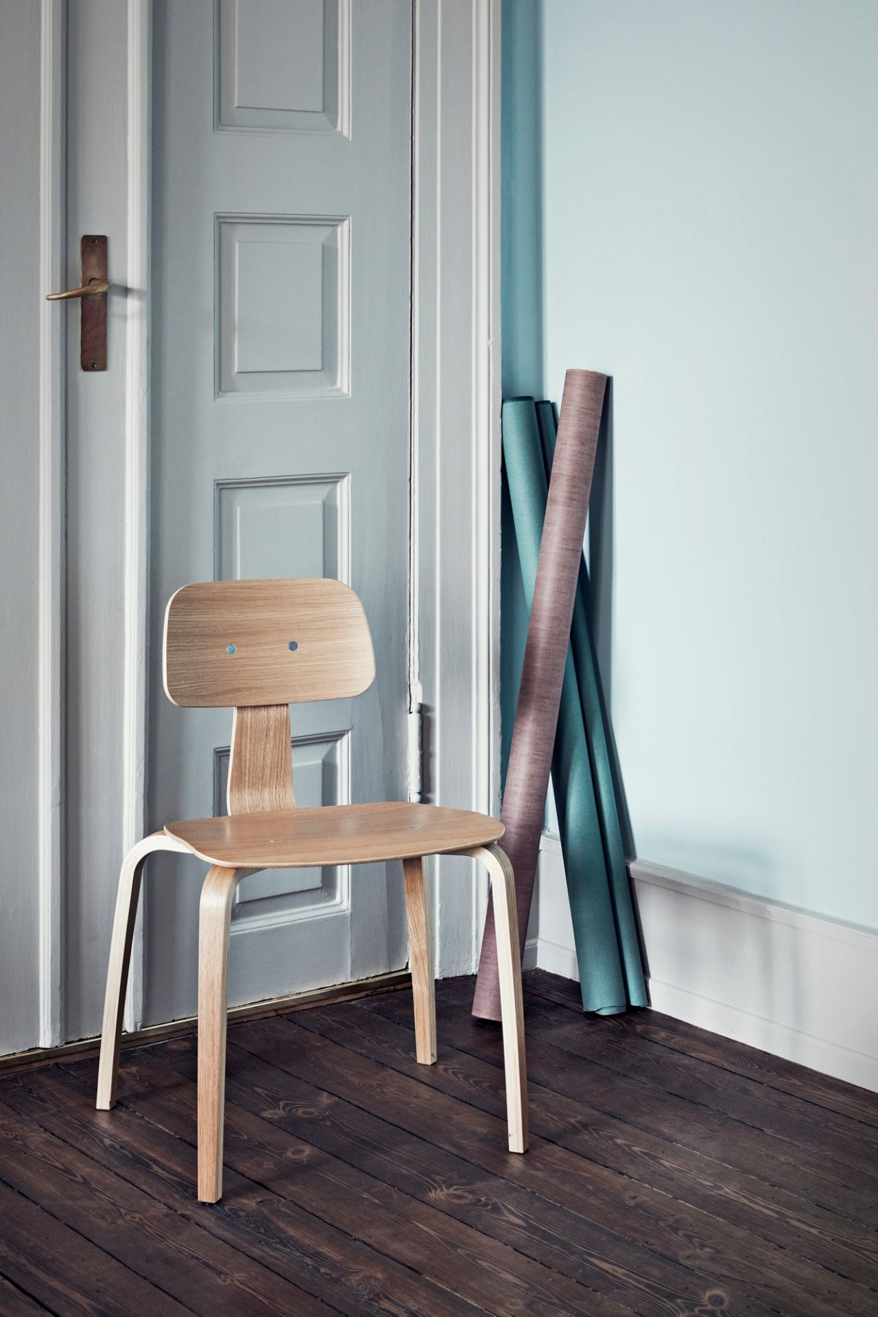 Kevi Stuhl mit Eichenholz-Sitz und Rückenlehne vor einer blauen Tür und Holzboden.