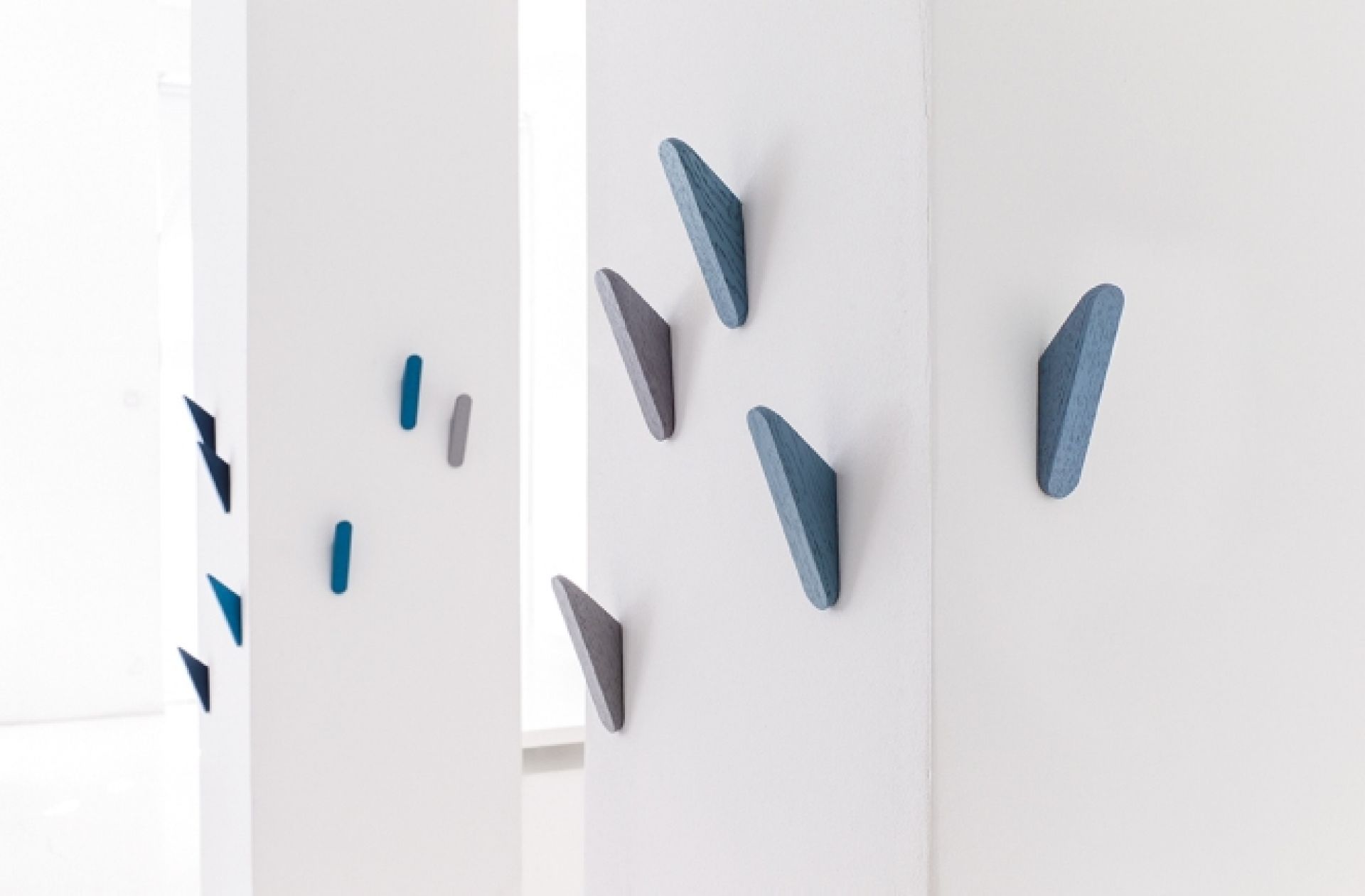 Cut Wandhaken von Schönbuch in Blau- und Grautönen an einer weißen Wand. Moderne Garderobenhaken.