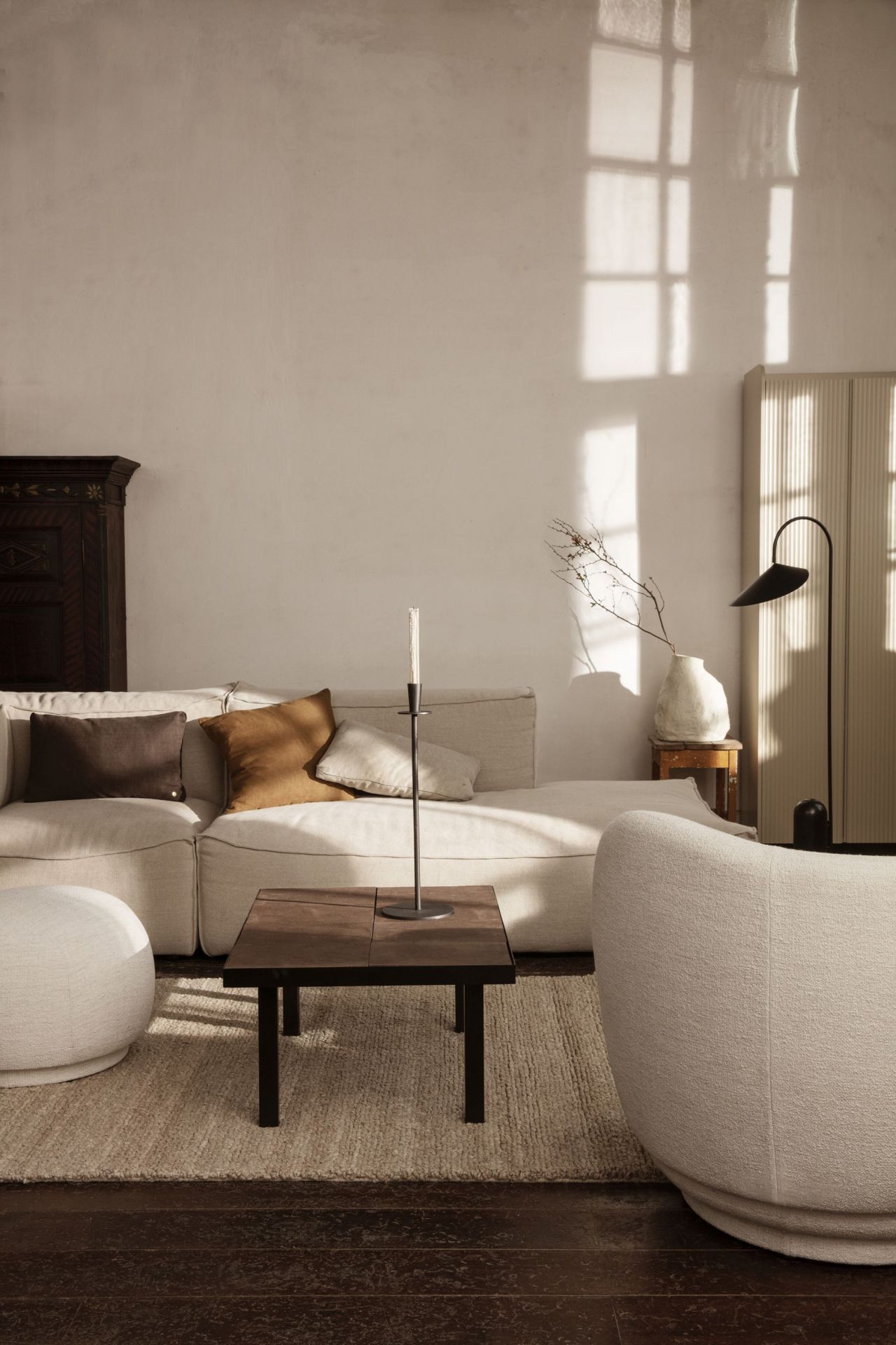 Beige Wohnzimmer-Szene mit Rico Pouf von Ferm Living, Sofa, Teppich und Kerzenständer.