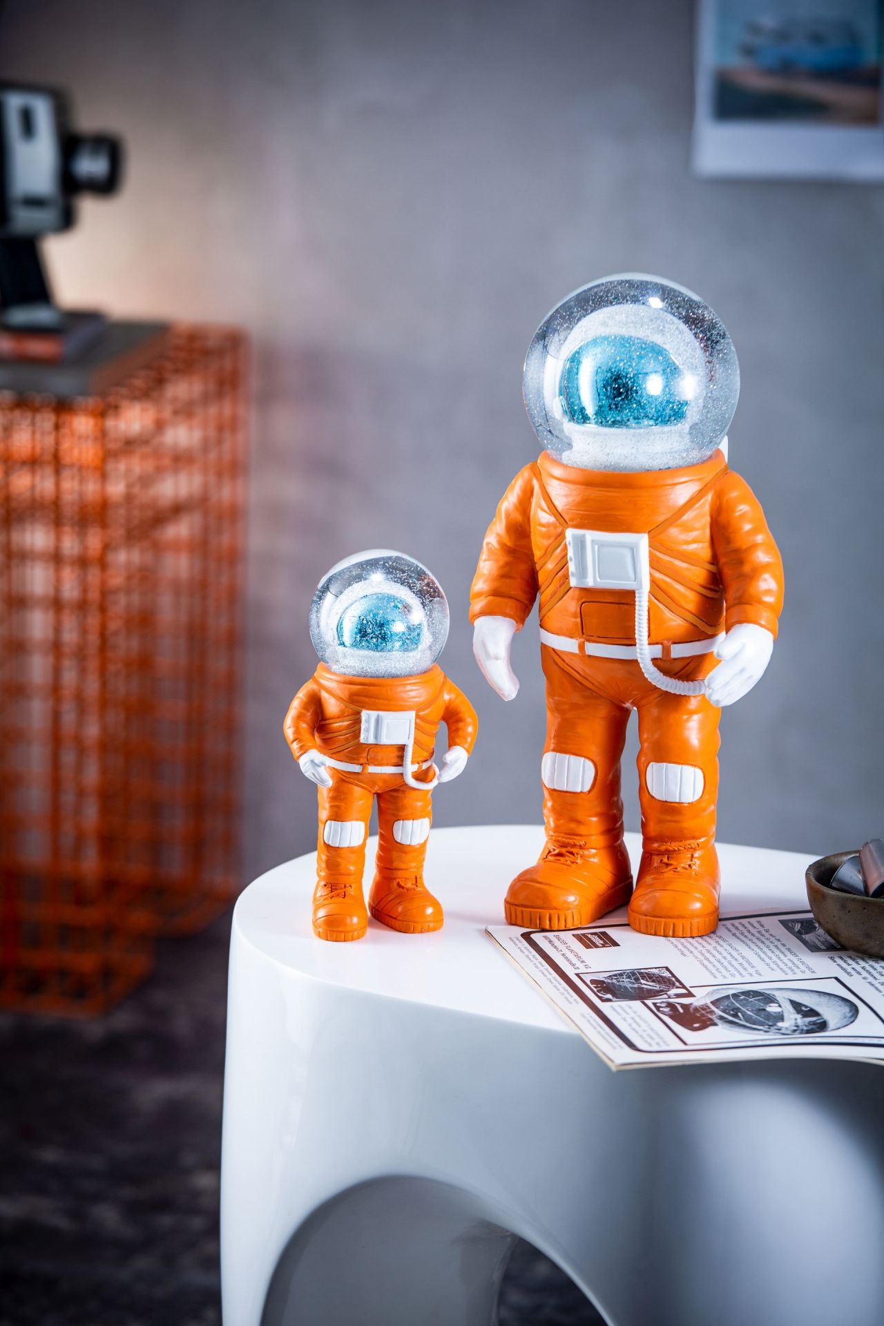 Zwei orangefarbene Marstronaut Glitzerkugeln von Summerglobes, Einzelstücke, auf einem weißen Tisch. Dekorative Schneekugel mit Astronauten.