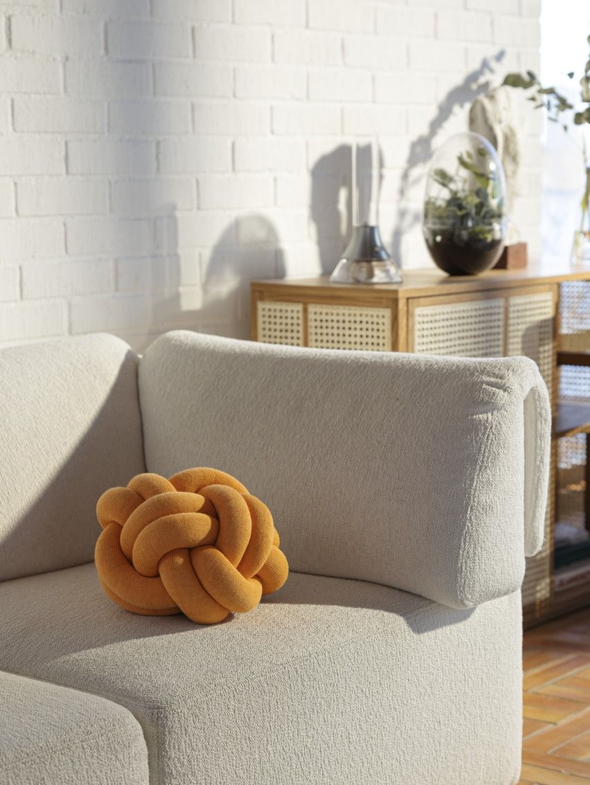 Orangefarbenes Knot Kissen von Design House Stockholm auf einem beigen Sofa, dekoratives Wohnaccessoire.