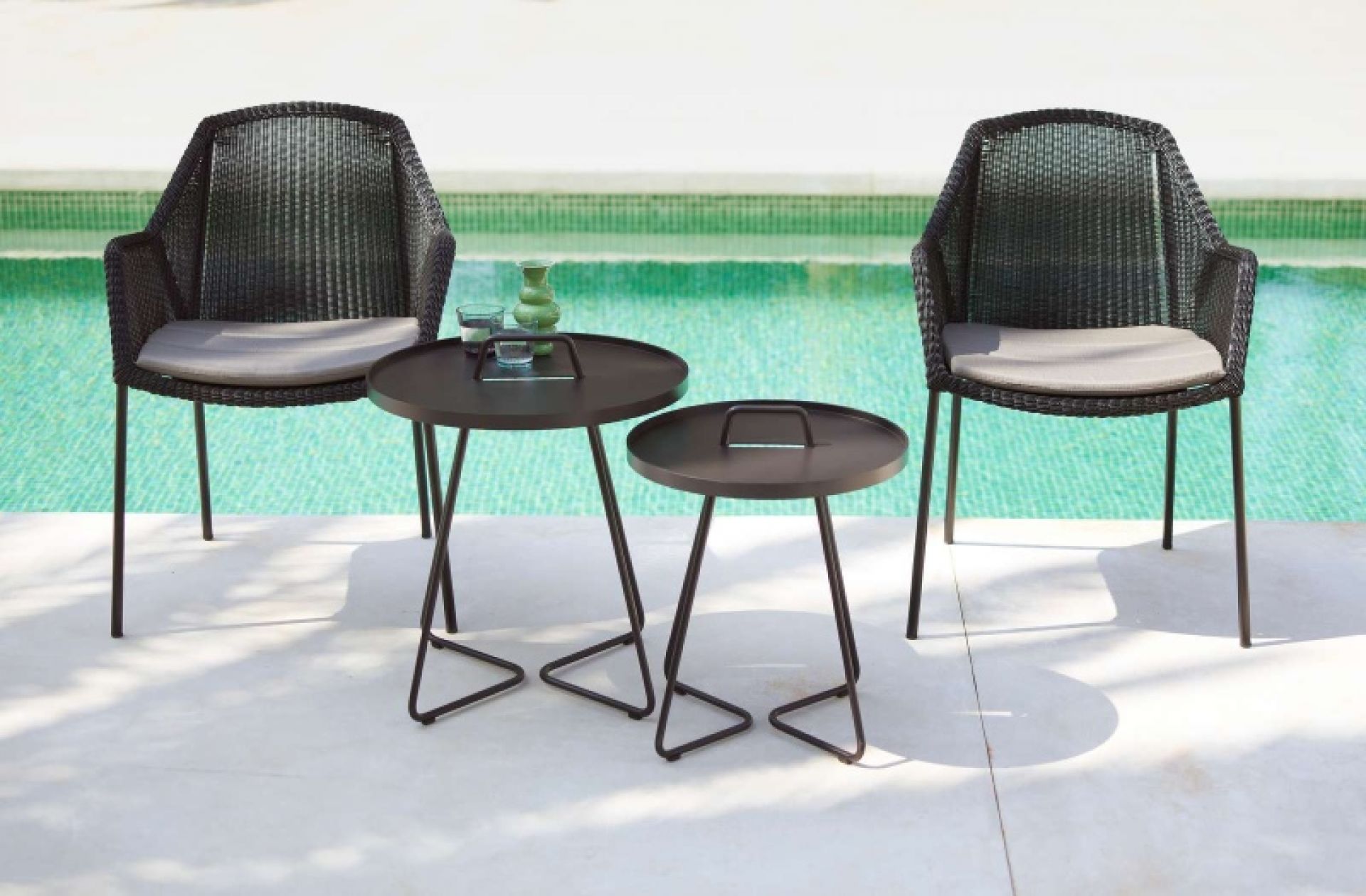 Cane-Line Breeze Outdoor Stuhl mit Kissen und Beistelltischen am Pool.