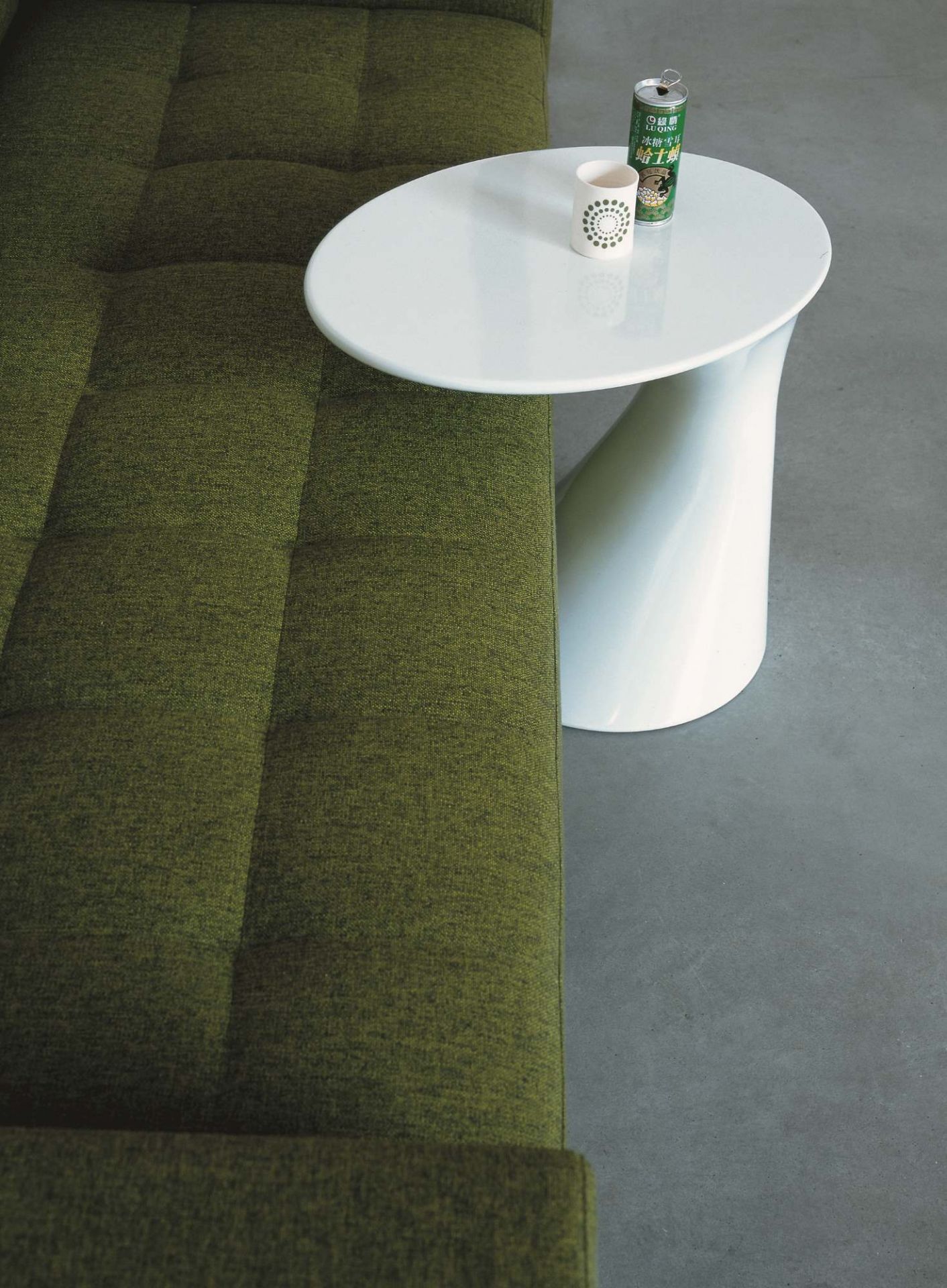 Detailaufnahme des Zanotta Tod Couchtischs mit Getränken auf einer weißen, runden Tischplatte neben einem grünen Sofa.