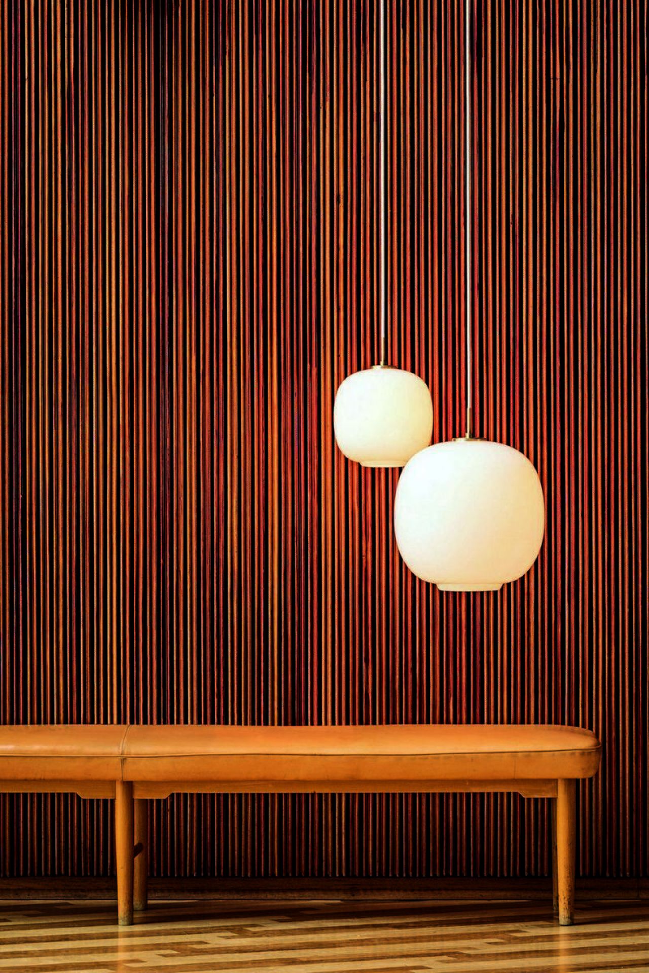 Zwei VL45 Radiohus Pendelleuchten von Louis Poulsen, weiße Glaslampen hängen vor einer Holzvertäfelung und einer Bank.