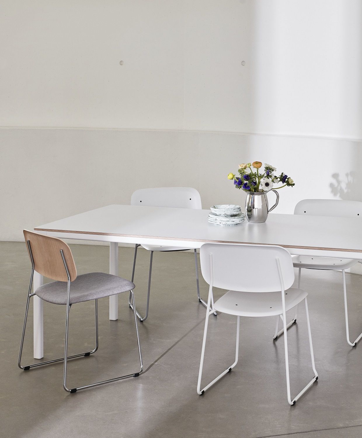 Esstisch mit vier Hay Soft Edge Stühlen, davon einer mit grauem Sitzpolster und Holzlehne.