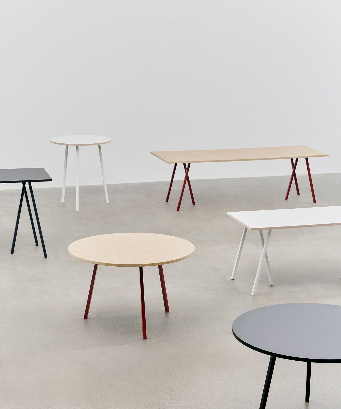 Mehrere Loop Stand Tische von Hay, darunter ein runder Esstisch mit Holzplatte und farbigen Beinen.