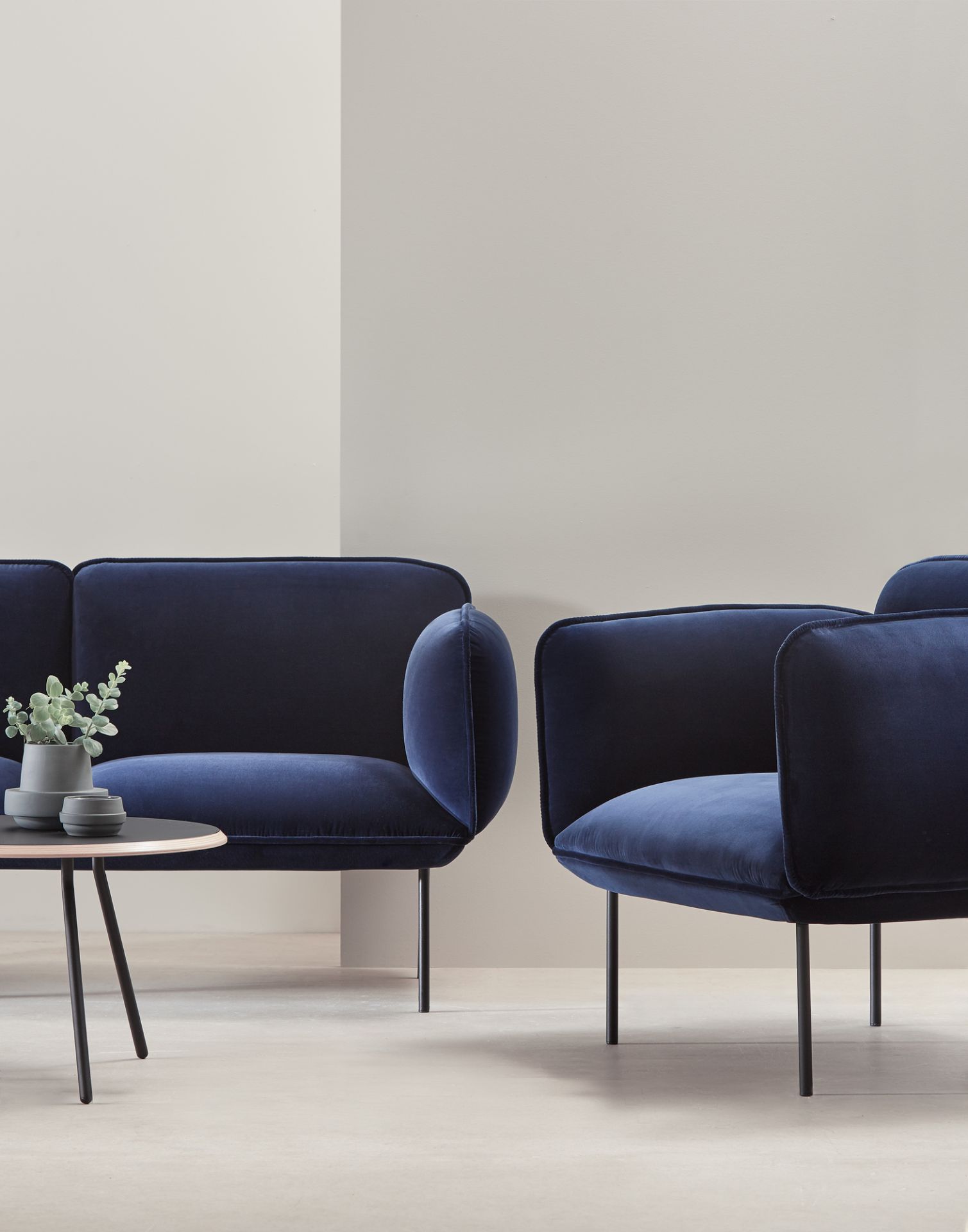 Soround Couchtisch von Woud neben blauen Samtsofas. Moderner runder Couchtisch mit Pflanze.