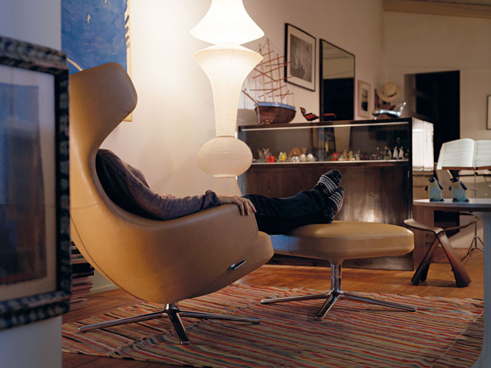 Person entspannt im beigen Vitra Grand Repos Sessel mit Hocker im Wohnzimmer.