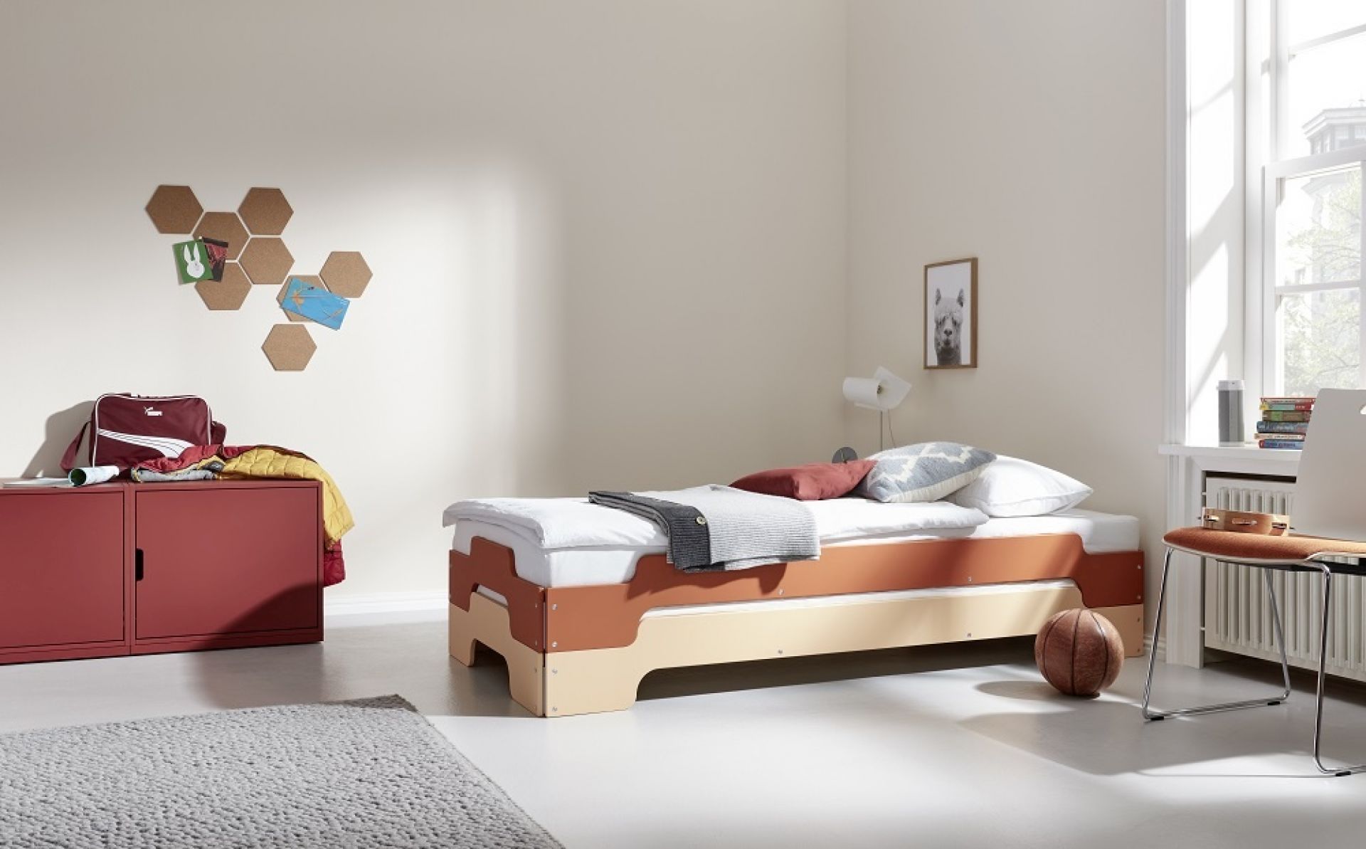 Helles Kinderzimmer mit Müller Möbelwerkstätten Stapelliege Klassik, Bettwäsche und rotem Schrank.