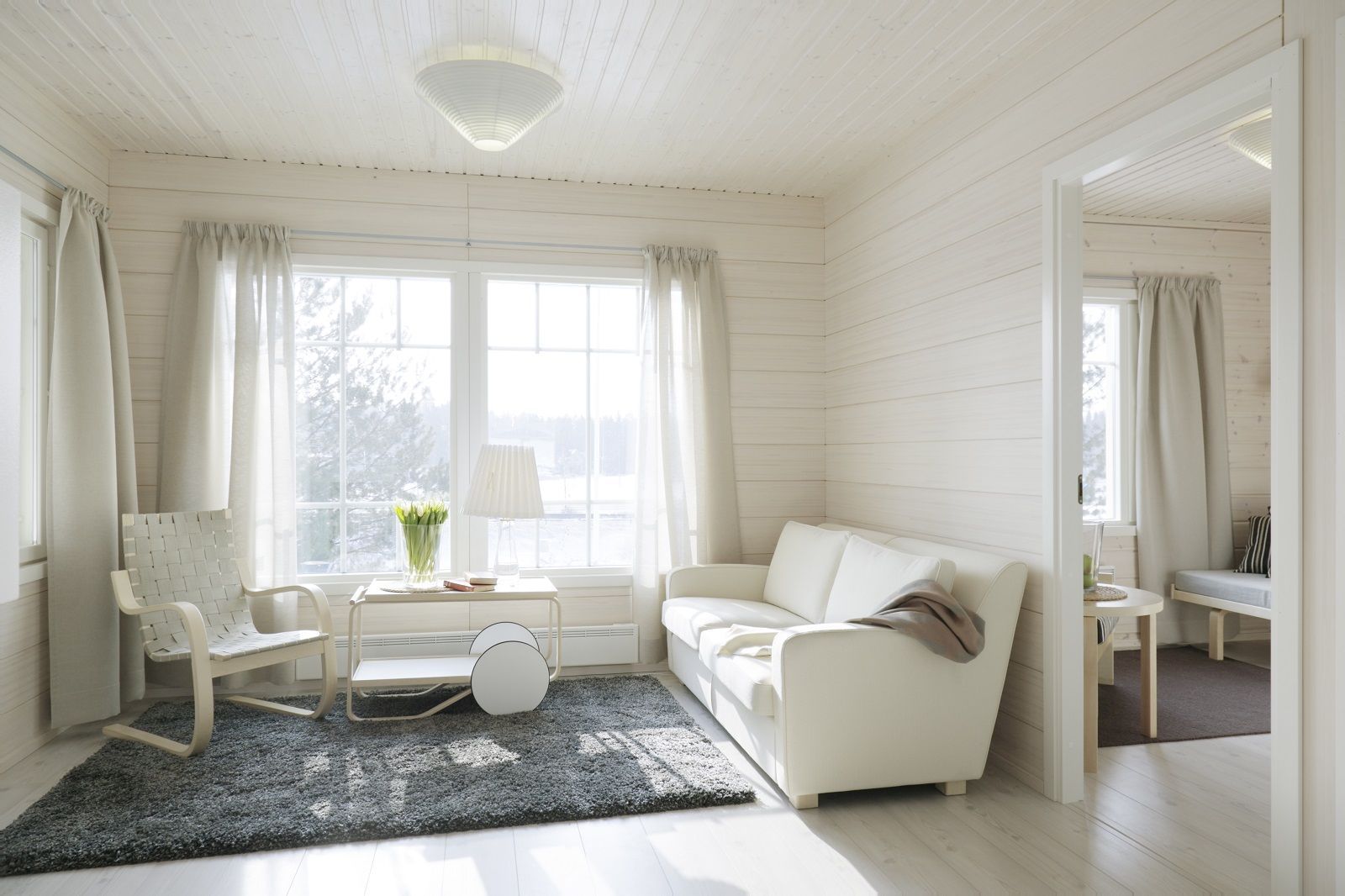 Heller Wohnraum mit Artek Sessel 406, Sofa, Teppich und Fenster mit Tageslicht. Skandinavisches Design.