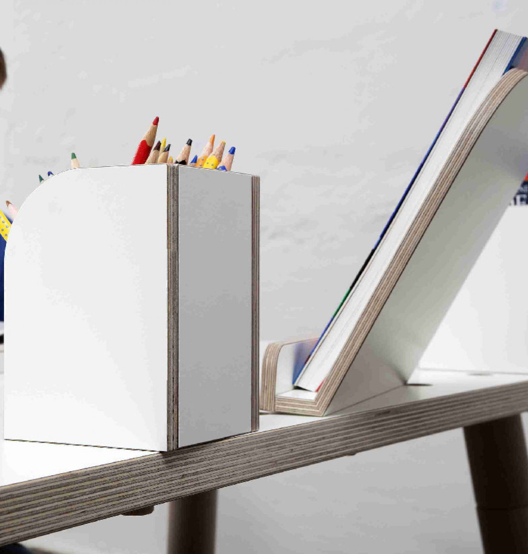 Weiße Growing Table Stiftebox für Kindertisch mit Buntstiften und Buchstütze auf einem Tisch.