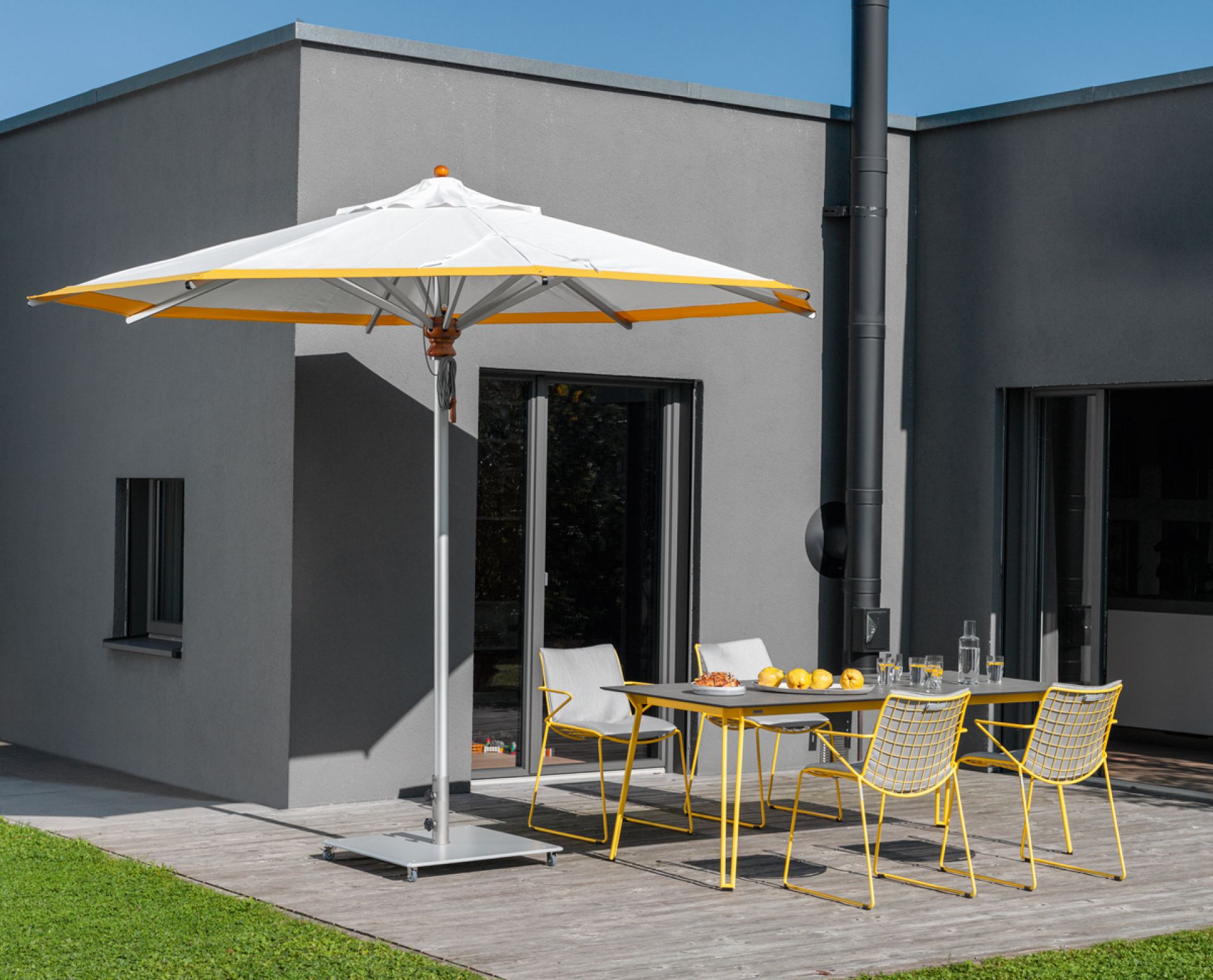 Alusonnenschirm rund sandfarben von Weishäupl spendet Schatten über einer modernen Gartensitzgruppe mit gelben Stühlen.