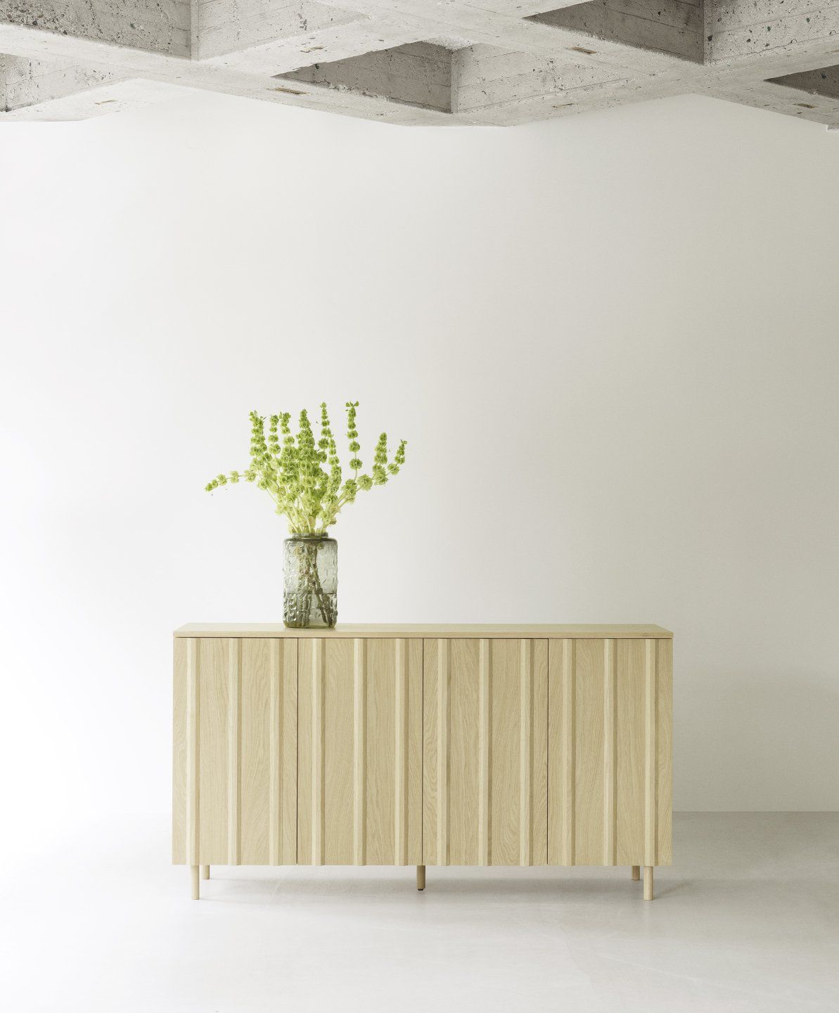 Helles Rib Sideboard von Normann Copenhagen mit geriffelten Türen und Vase mit grünen Blumen.