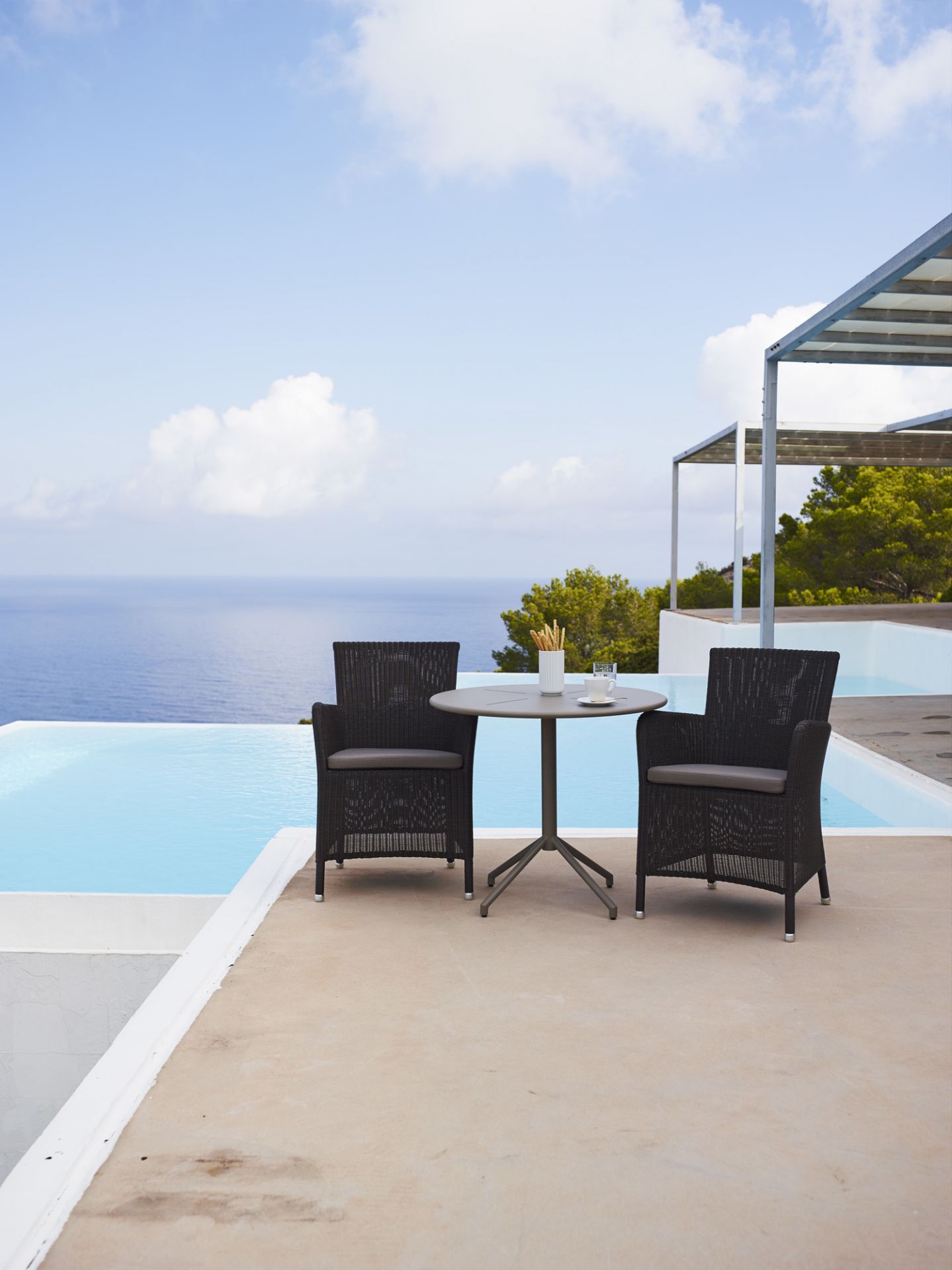 Schwarzer Hampsted Outdoor Sessel von Cane-Line am Pool mit Tisch und Meerblick. Gartenmöbel.