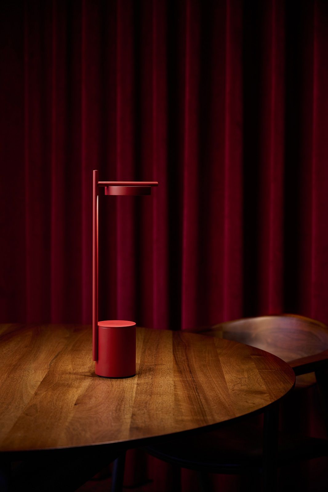 Rote Igram Akku Tischleuchte von Grupa auf Holztisch vor rotem Vorhang.