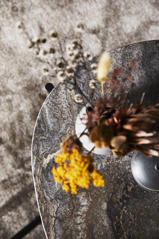 Detailaufnahme des grauen Woud Tint Rug Teppichs mit abstraktem Muster, kombiniert mit einem Beistelltisch und Trockenblumen.