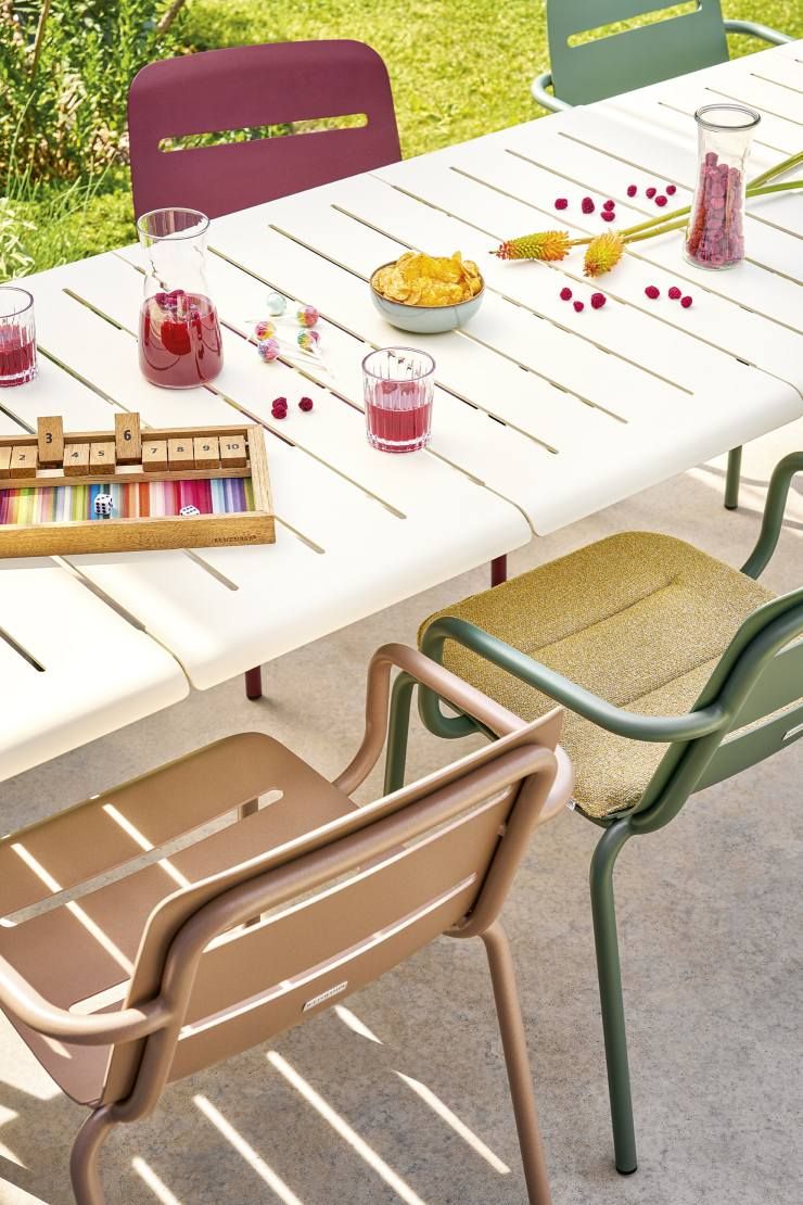 Weishäupl Vapio Sessel Outdoor mit Armlehne in verschiedenen Farben an Gartentisch mit Getränken und Snacks.