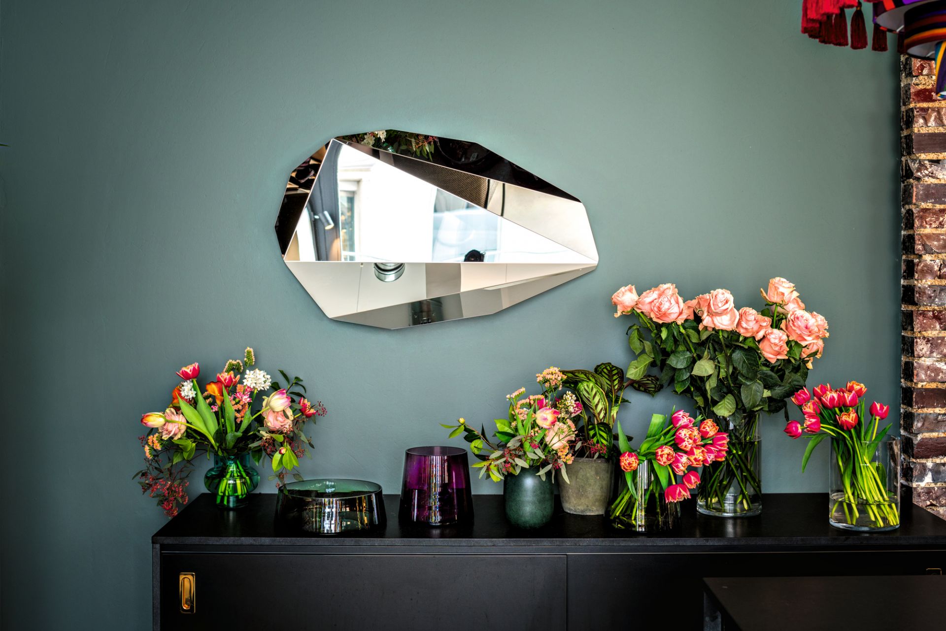 Piega Mirror Wandspiegel von Classicon, ein moderner Design-Spiegel in geometrischer Form an einer grünen Wand.