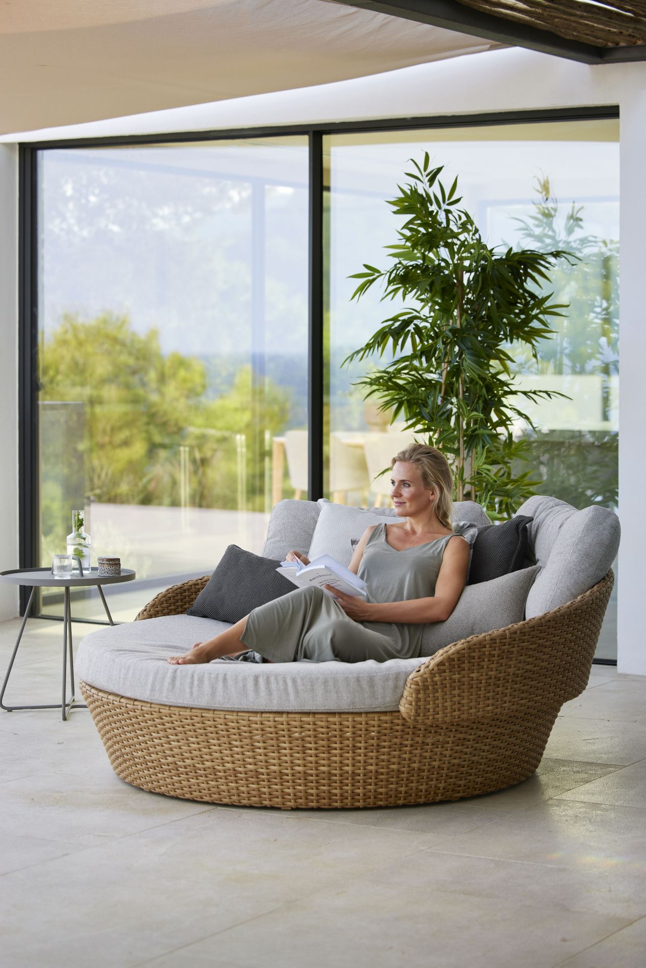 Frau entspannt auf Cane-Line Ocean Daybed aus Rattan mit Kissen im Freien.