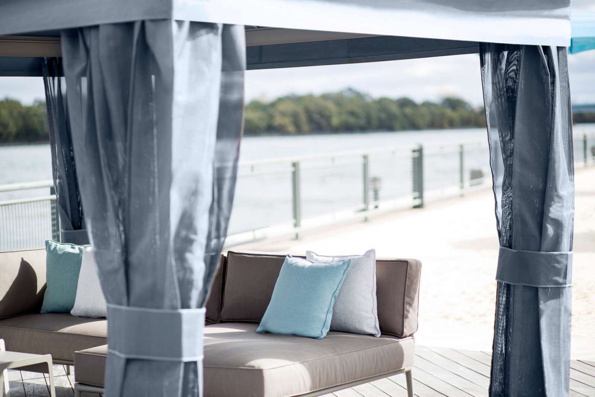 Cane-Line Conic Daybed Outdoor Schlafsofa mit Vorhängen und Kissen am Wasser.