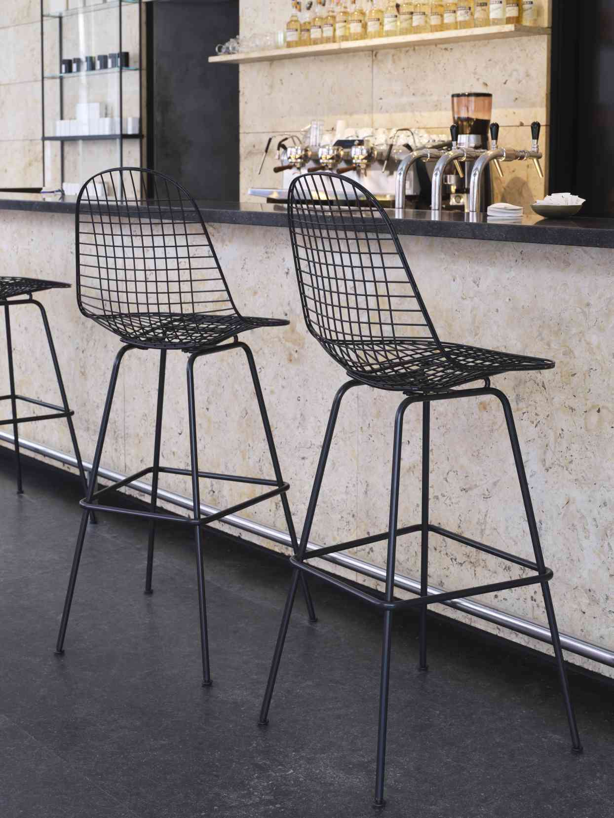 Schwarzer Eames Wire Bar Stool Barhocker von Vitra vor einer Bar, modernes Design, Sitzmöbel.
