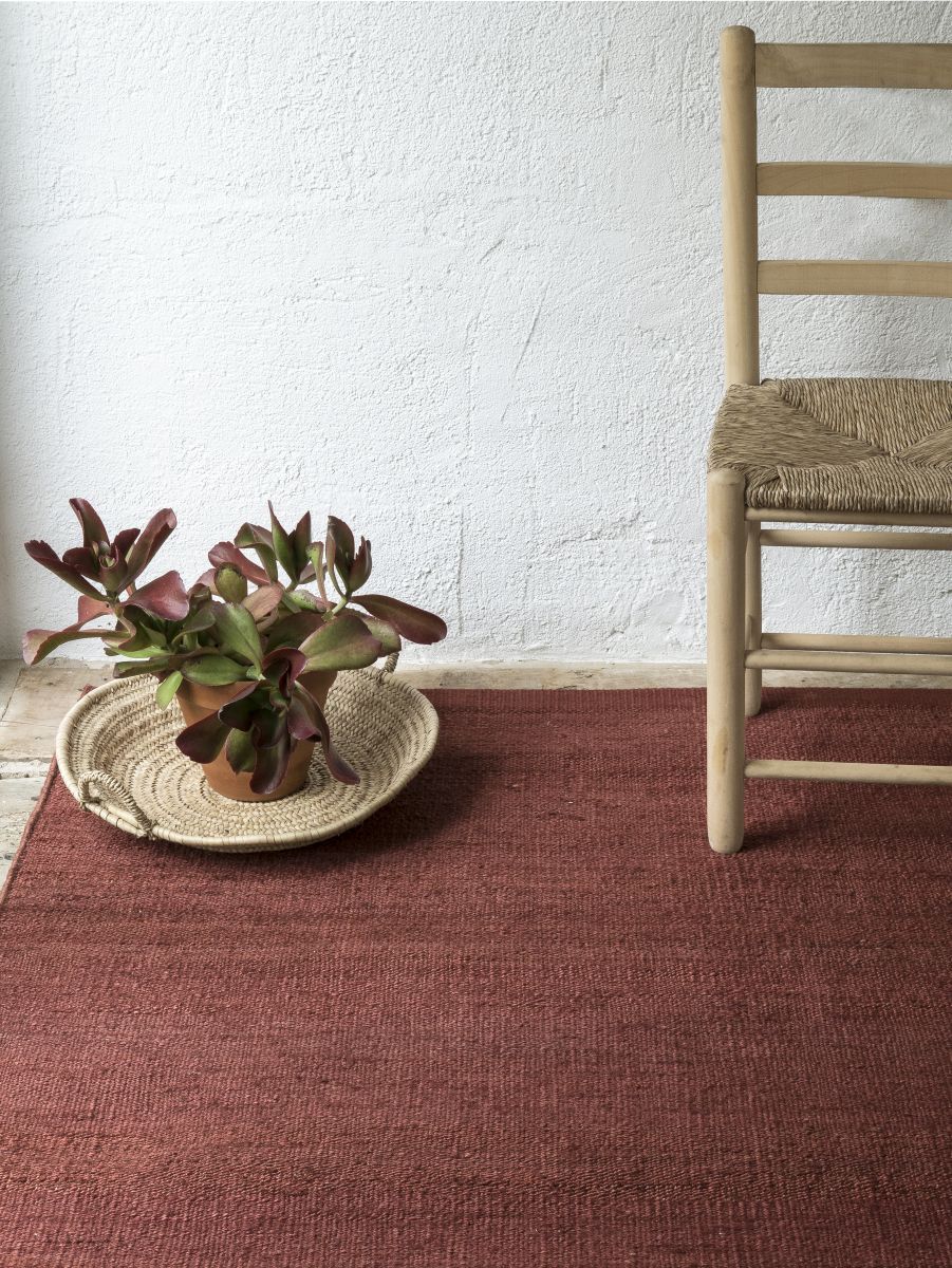 Nanimarquina Vegetal Teppich in Rotbraun, 200x300 cm, mit Pflanze und Holzstuhl auf dem Teppich.