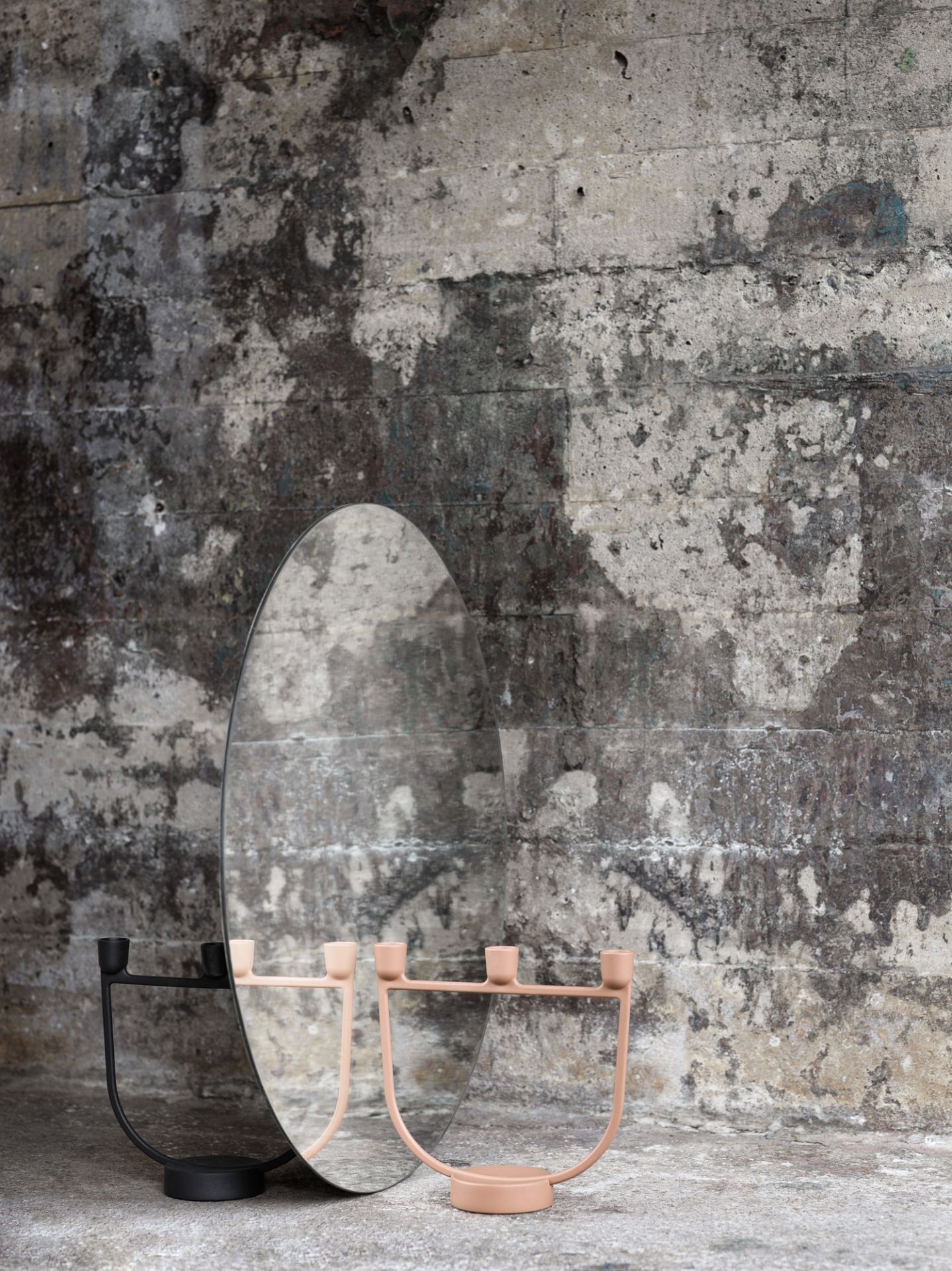 Muuto Open Candelabra Kerzenhalter in Schwarz und Rosa vor einem Spiegel und Betonwand.