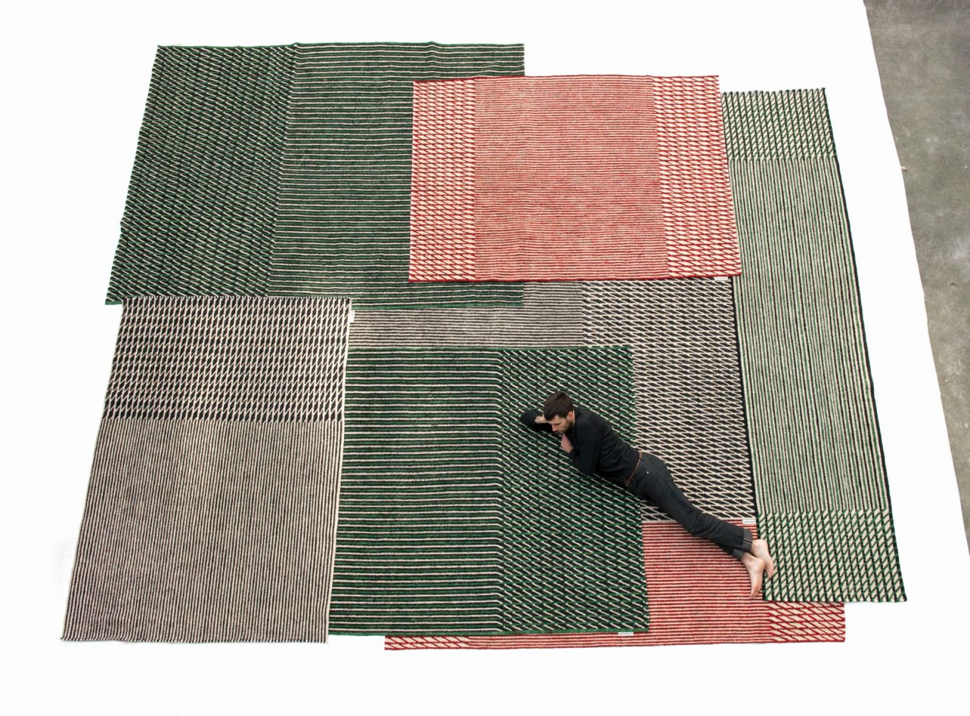 Mann liegt auf mehreren Nanimarquina Teppichen, Blur Läufer in Grün, Rot und Beige.