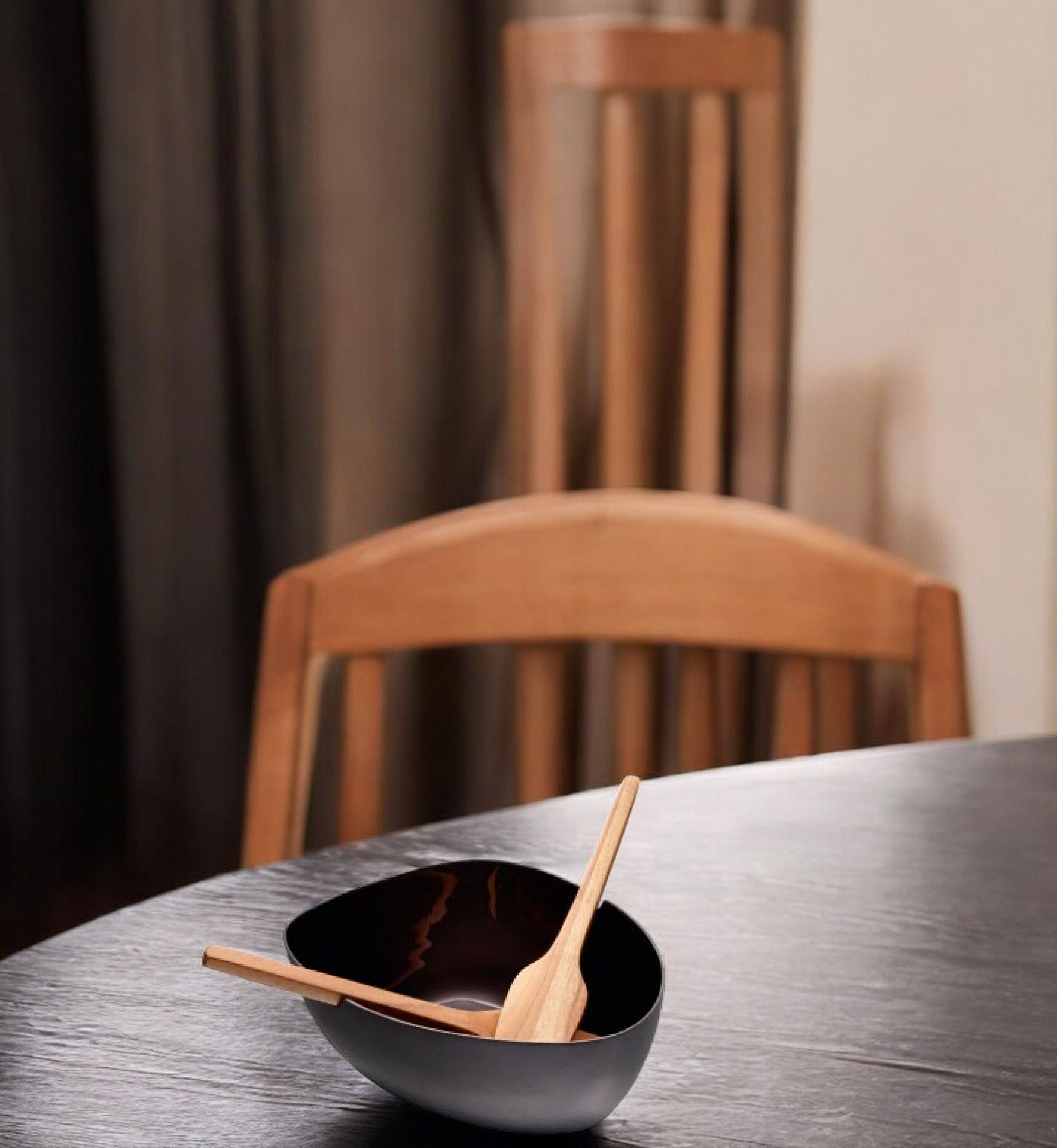 Schwarze Boat Salatschale von Philippi mit Holz Besteck auf einem dunklen Holztisch.