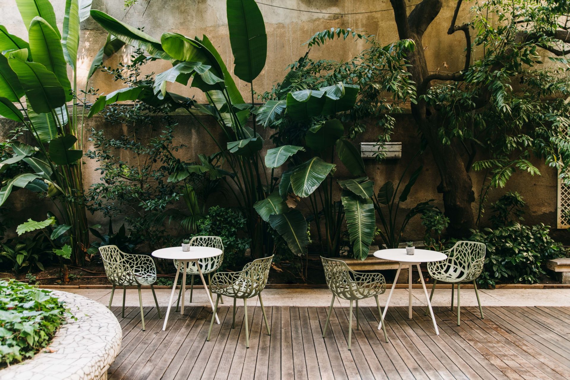 Pulvergraue Forest Outdoor Sessel mit filigranem Design auf einer Holzterrasse vor üppigem Grün.