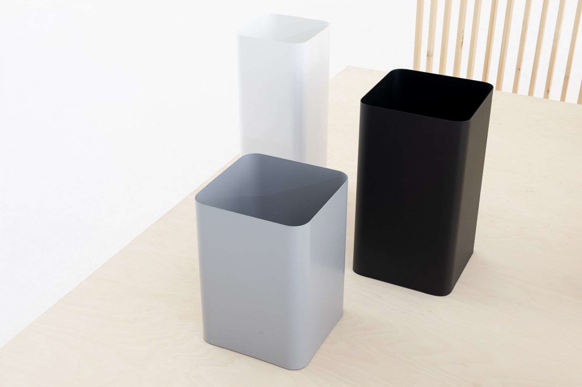 Drei Flow II Papierkörbe von Cascando in Grau, Weiß und Schwarz auf hellem Untergrund.