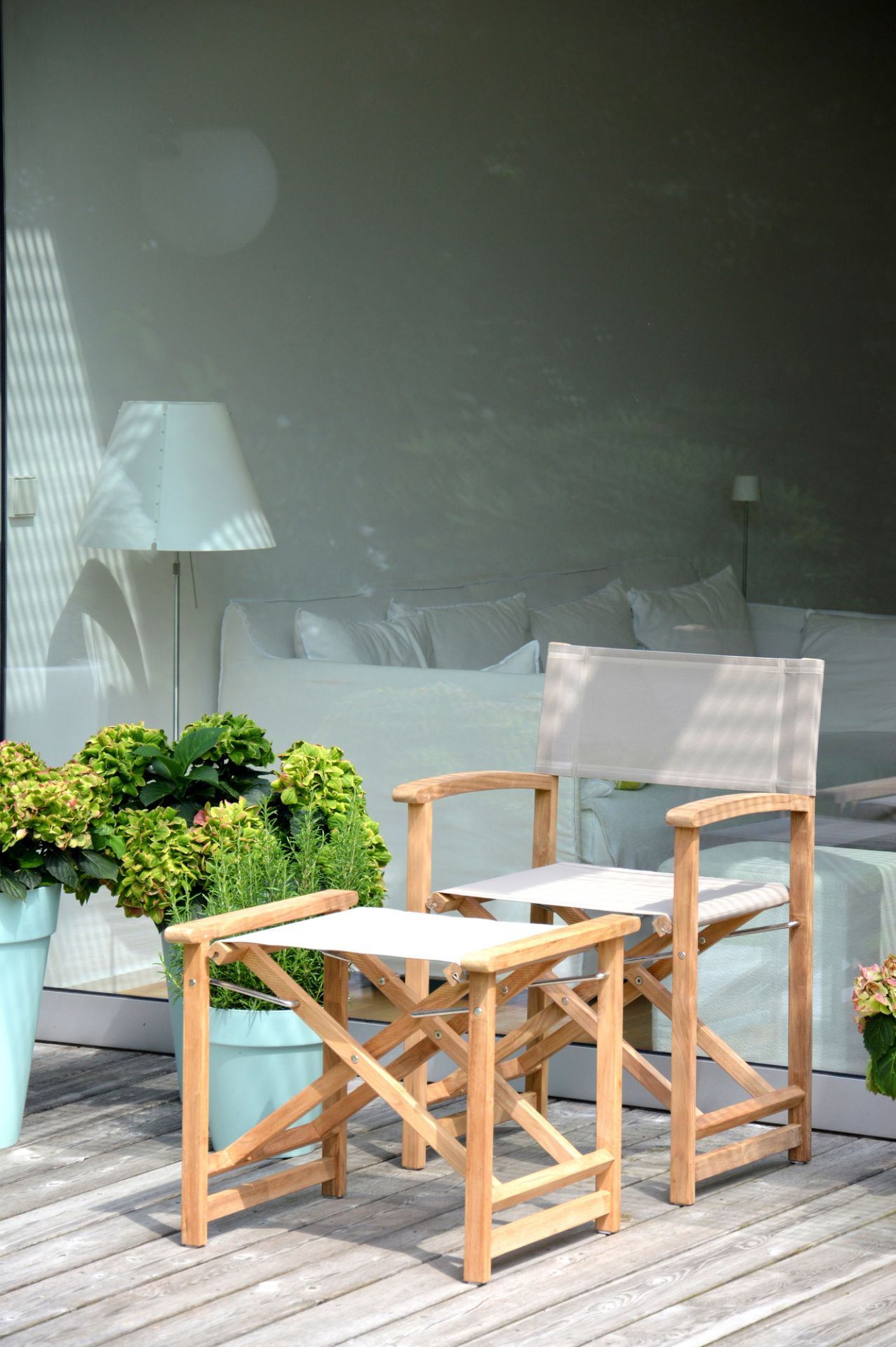 Urban Regiestuhl von Jan Kurtz mit taupefarbenem Bezug und passendem Hocker auf einer Holzterrasse.