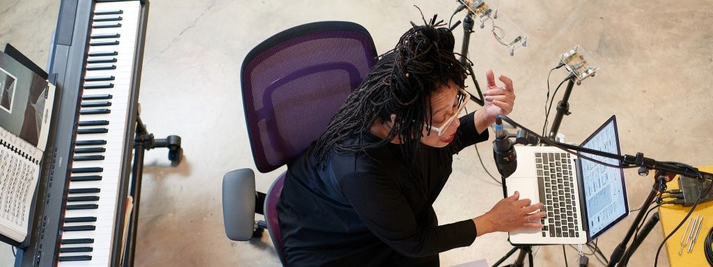 Draufsicht: Frau sitzt auf Steelcase Karman Bürostuhl, arbeitet am Laptop und singt.