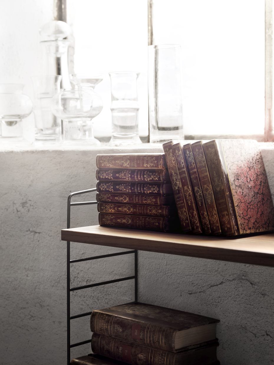 Nahaufnahme eines String Regalsystems mit dekorativen Büchern und Glasvasen vor einem Fenster.