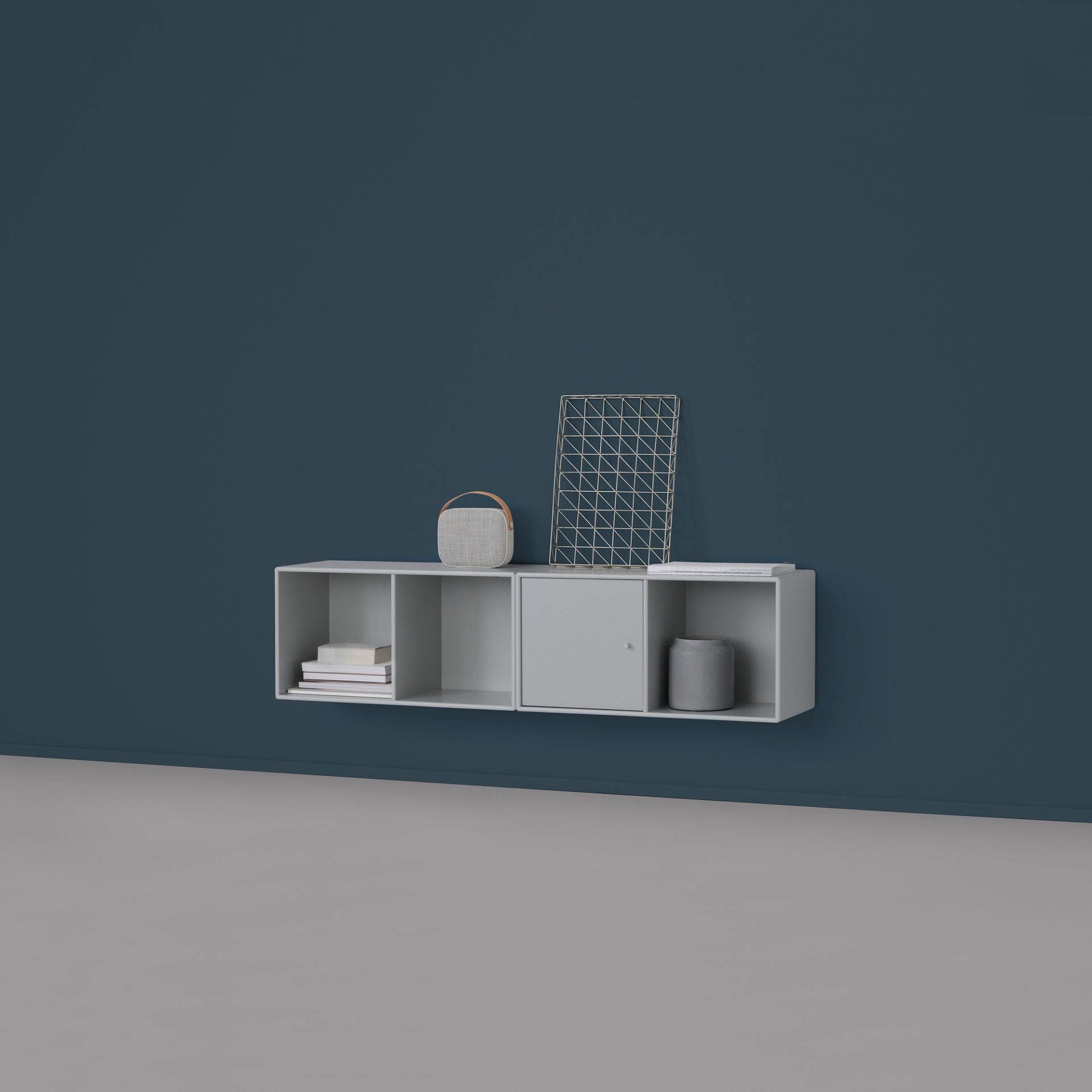 Graues Montana LINE Wandregal mit Tür, Fächern und Dekoration an einer blauen Wand.