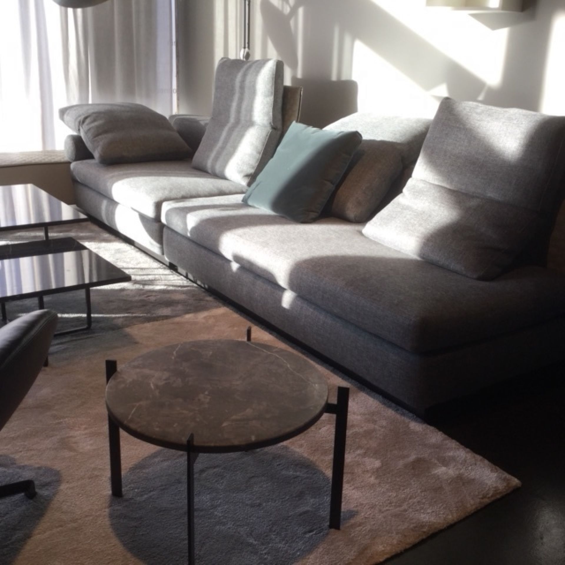 Single Deck Couchtisch von Ox Denmarq: Runder Marmortisch mit schwarzem Metallgestell vor grauer Couch.