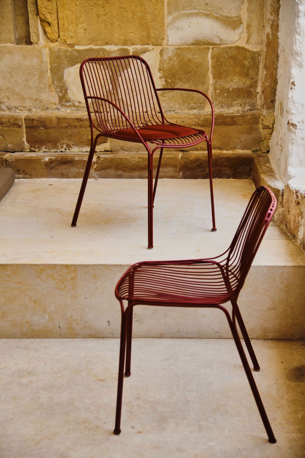Zwei rote Hiray Outdoor Stühle von Kartell vor einer Steinwand. Gartenmöbel und Design.