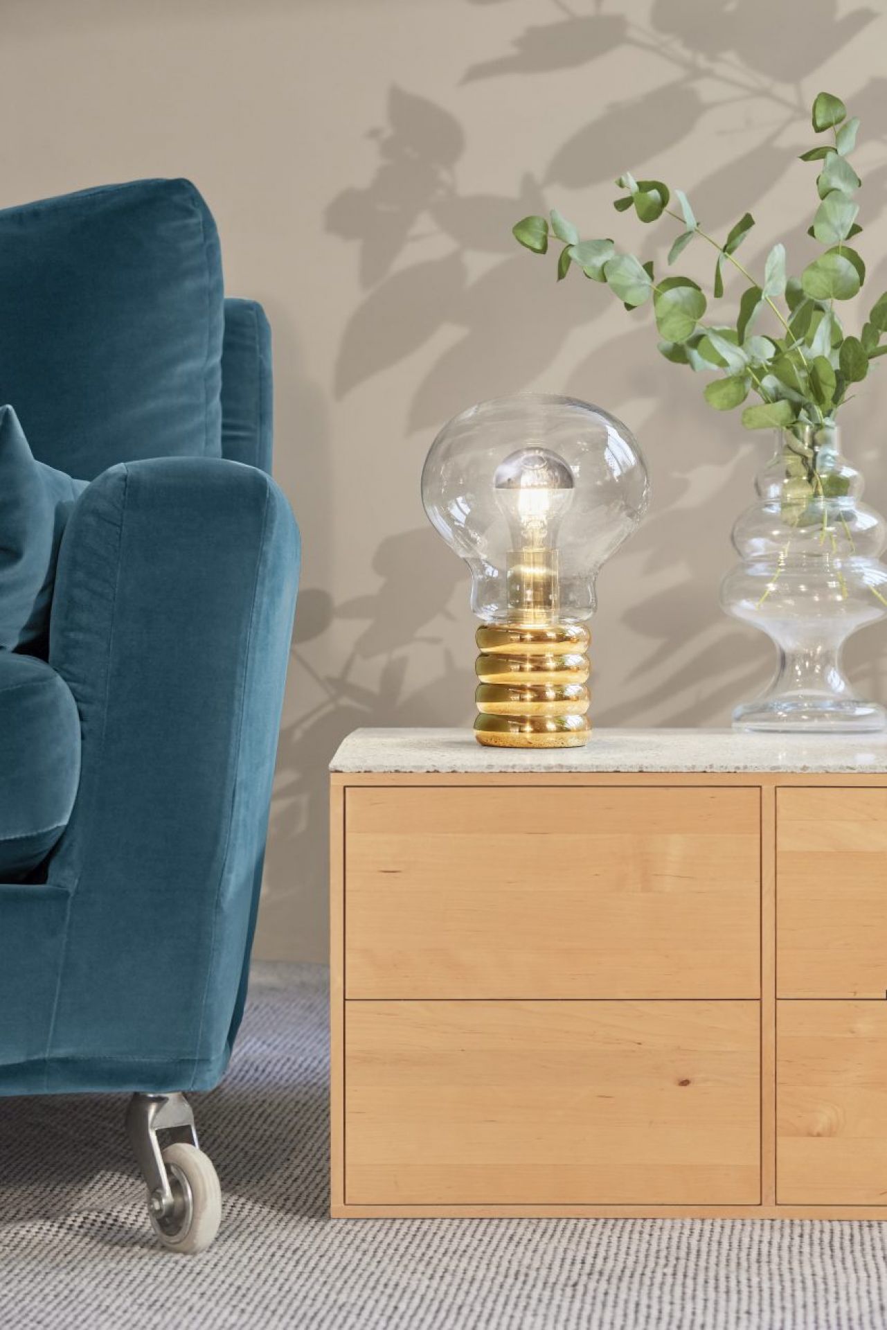 Ingo Maurer Bulb Tischleuchte aus Messing und Glas auf einem Nachttisch neben einem Sessel.