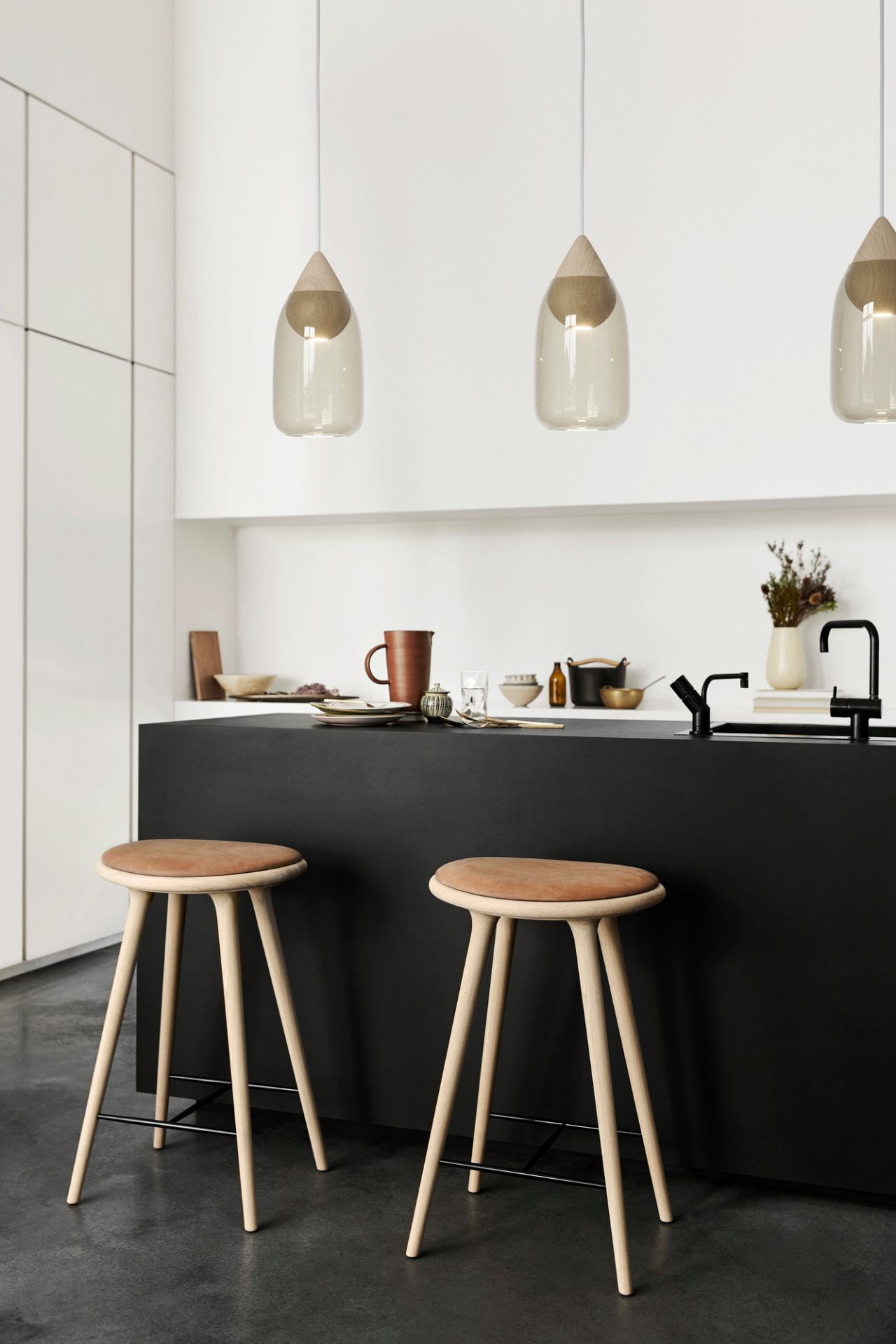 Zwei Stool Barhocker aus geseifter Eiche von Mater vor einer schwarzen Kücheninsel.