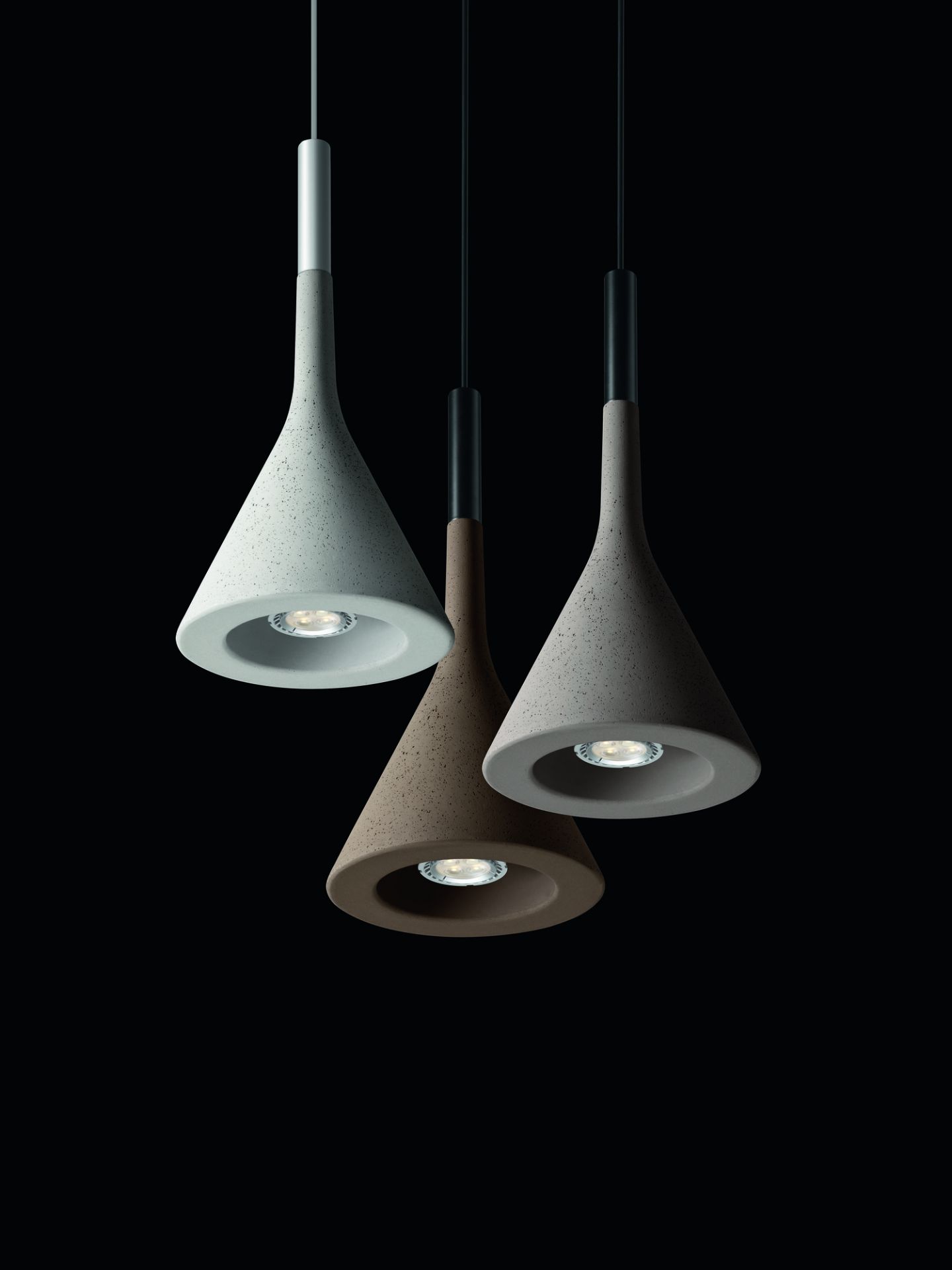Drei Aplomb Pendelleuchten von Foscarini in Grau und Braun vor schwarzem Hintergrund.