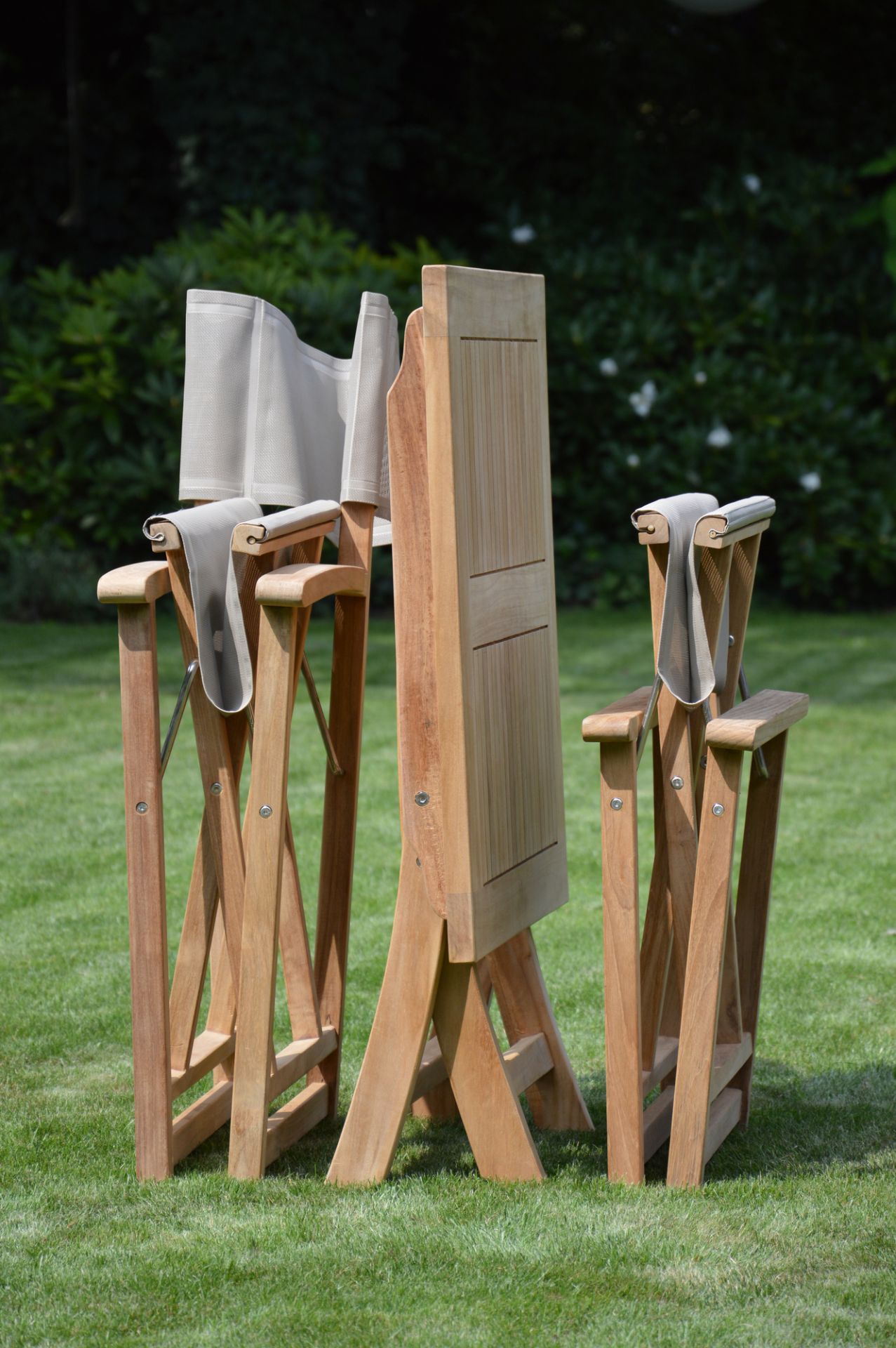 Zusammengeklappter Urban Regiestuhl von Jan Kurtz mit taupefarbenem Bezug auf Rasen, Gartenmöbel aus Teakholz.