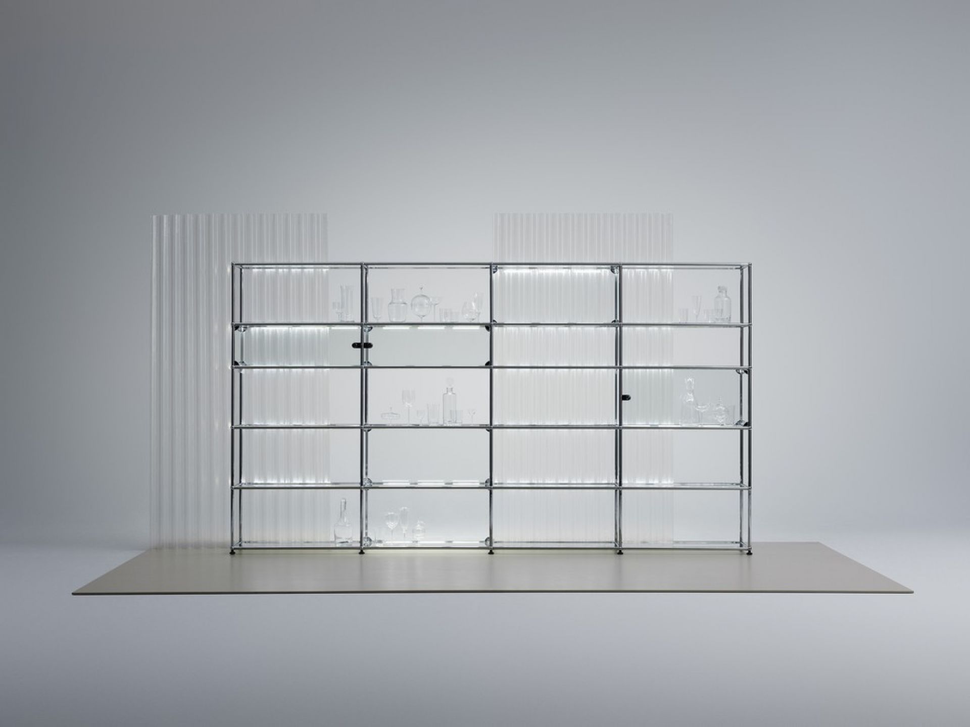 USM Haller E Regal mit integrierter, dimmbarer Beleuchtung, Glasböden und Chromgestell im minimalistischen Design.