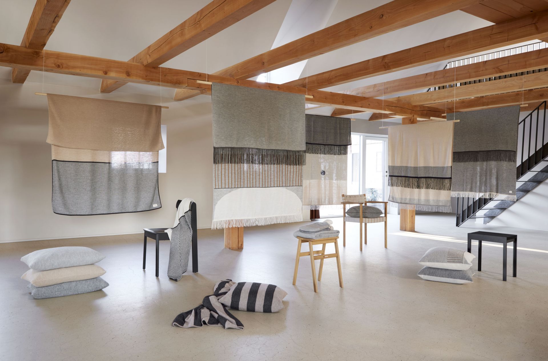 Aymara Decken in verschiedenen Designs und Farben hängen im Raum, ergänzt durch Kissen und Stühle.